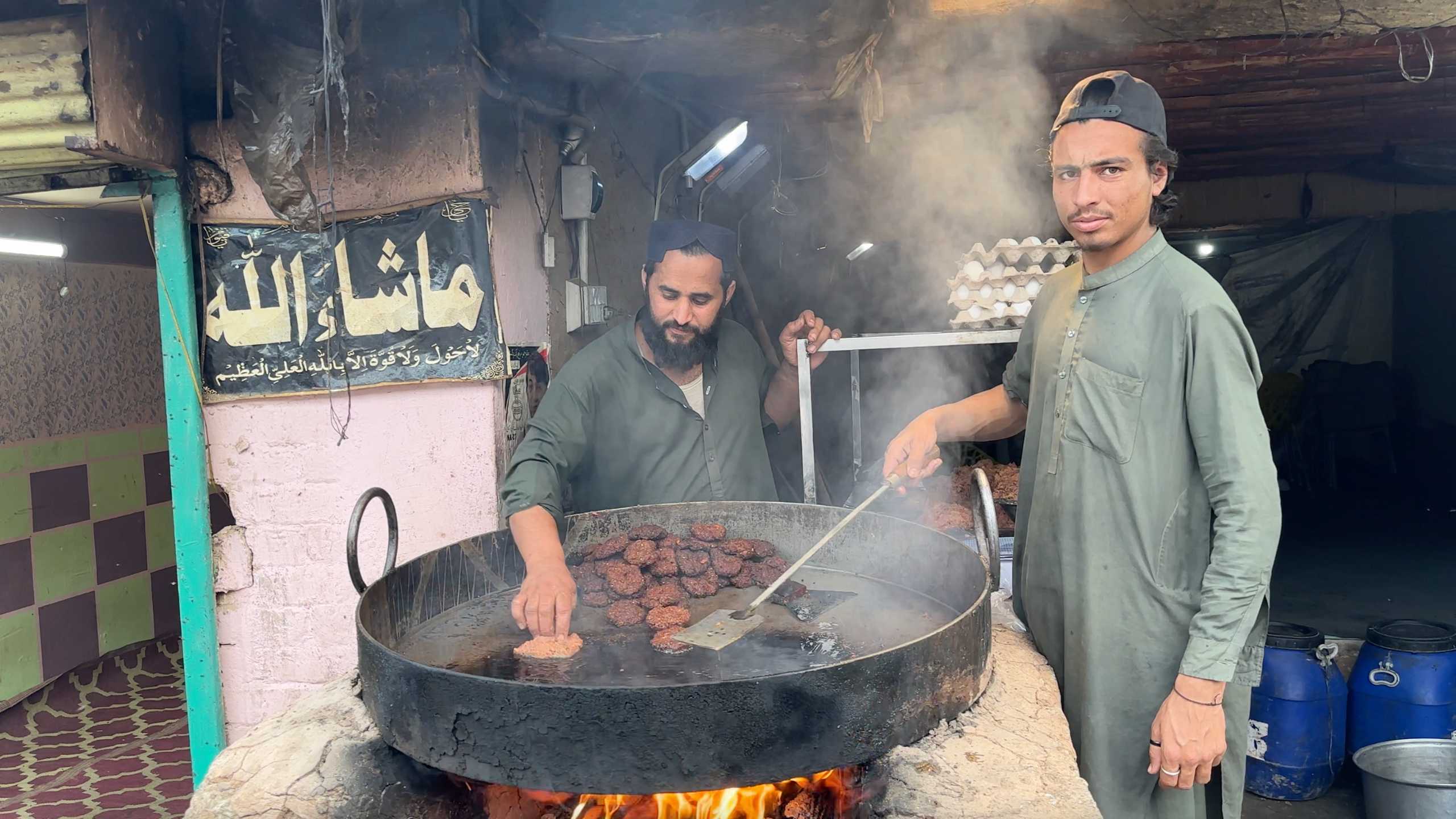 Cooks prepare fried snacks in a large cauldron, the market bustling with activity around them.