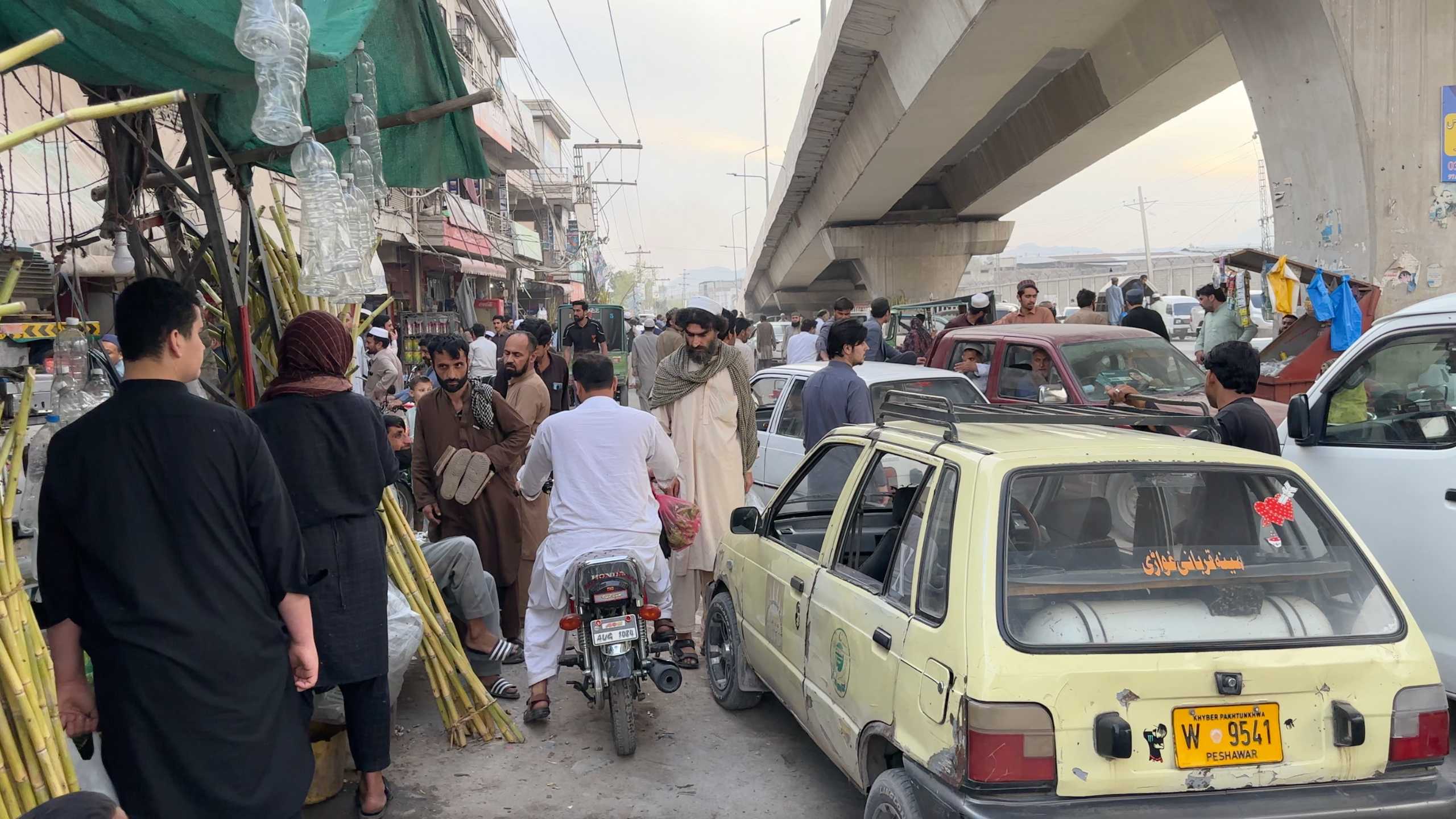 A crowded street scene with vehicles and pedestrians navigating the market.