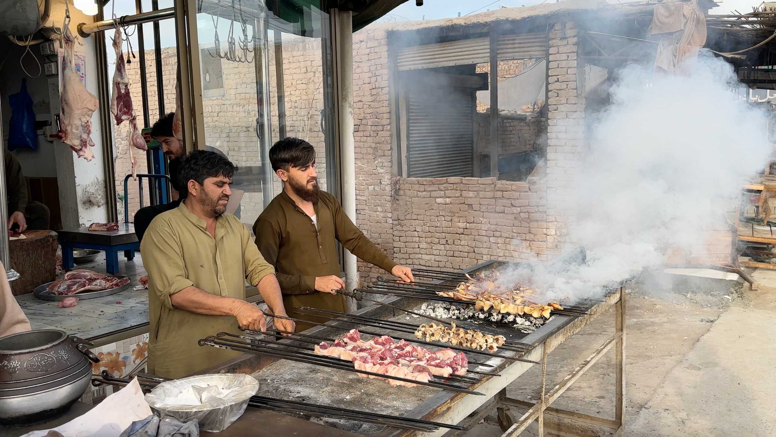 Skilled chefs grill assorted meat skewers over open flames, the air thick with smoke.