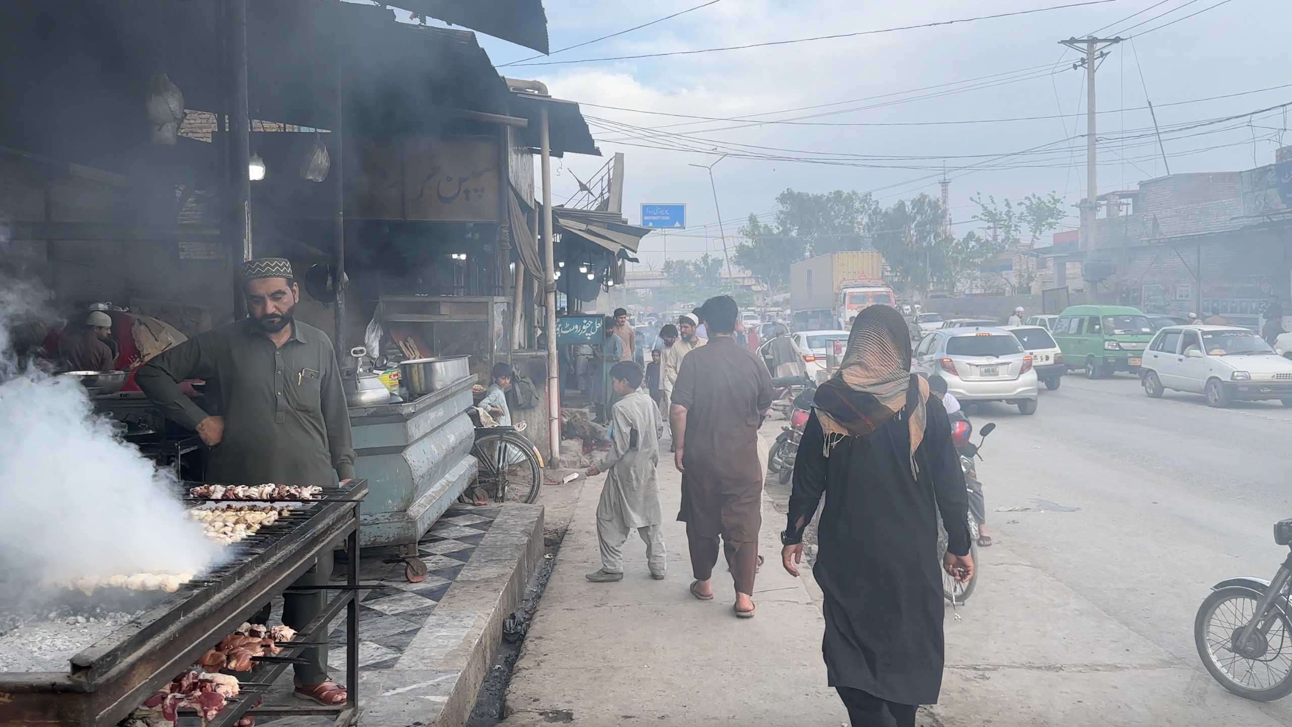 Shoppers walk through the smoky market street, where fresh meat is grilled and sold.