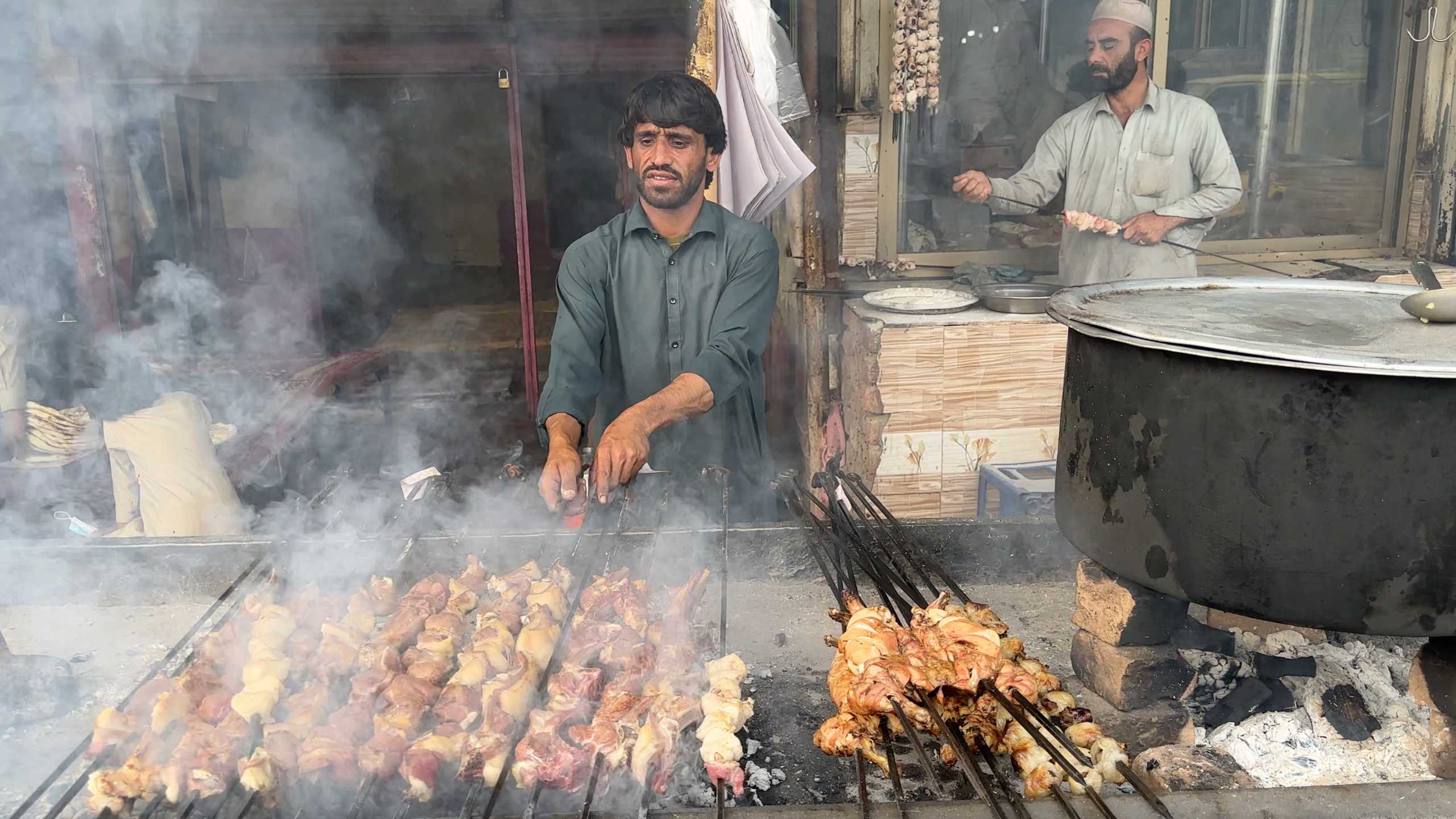 A man tends to a large grill, skewers lined with juicy meats cooking over hot coals.