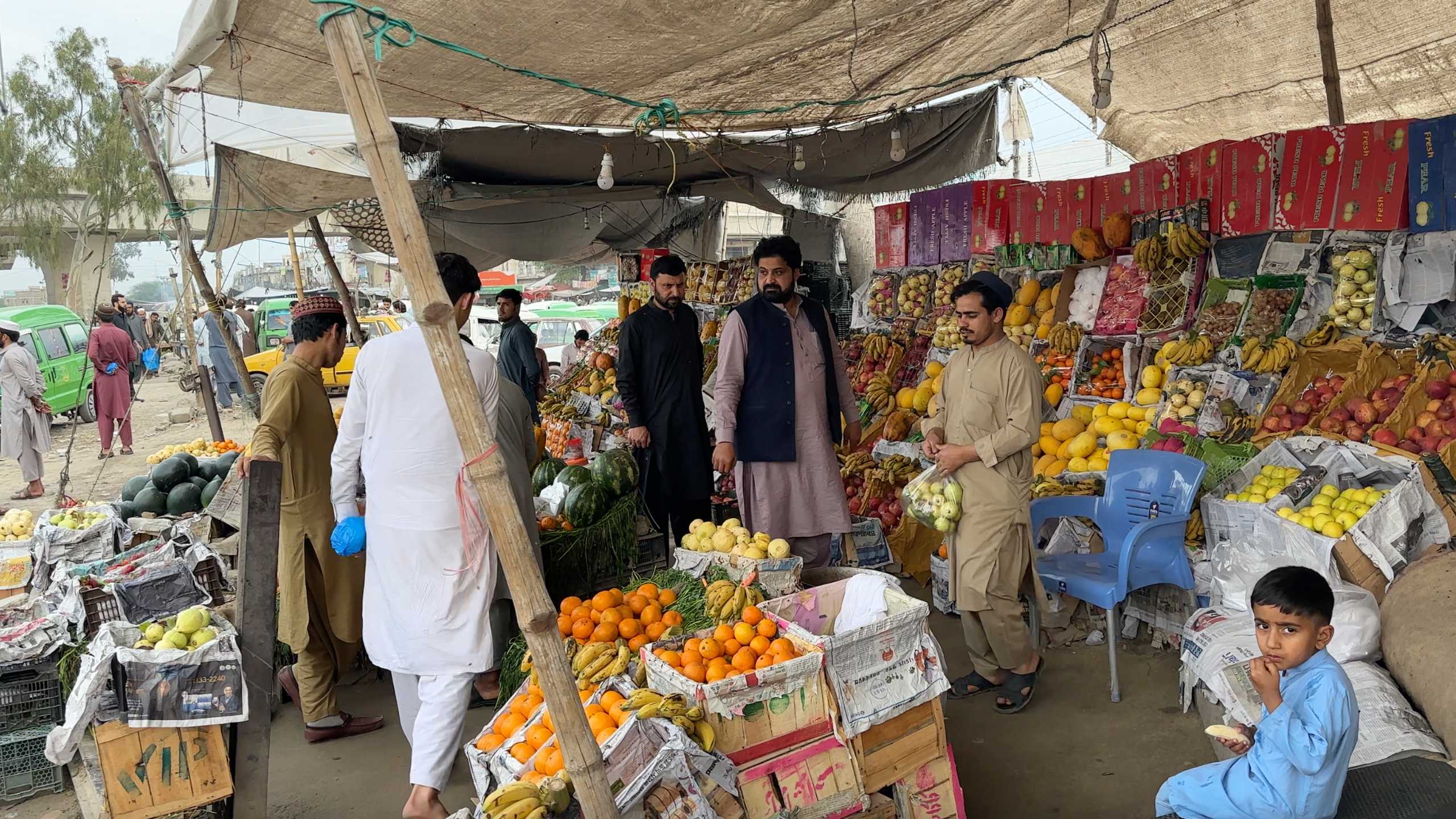 A busy produce stall with fruits and vegetables draws in locals for their daily shopping.