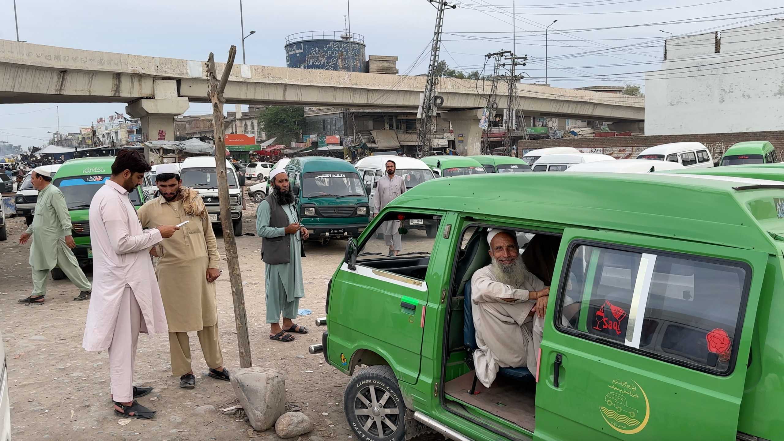 Local transport vans await passengers as drivers chat nearby in the market’s busy atmosphere.