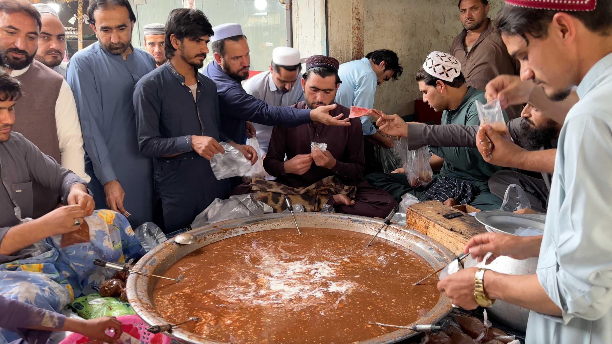 Men gather around a large pot, preparing a local dish as customers eagerly await their orders.