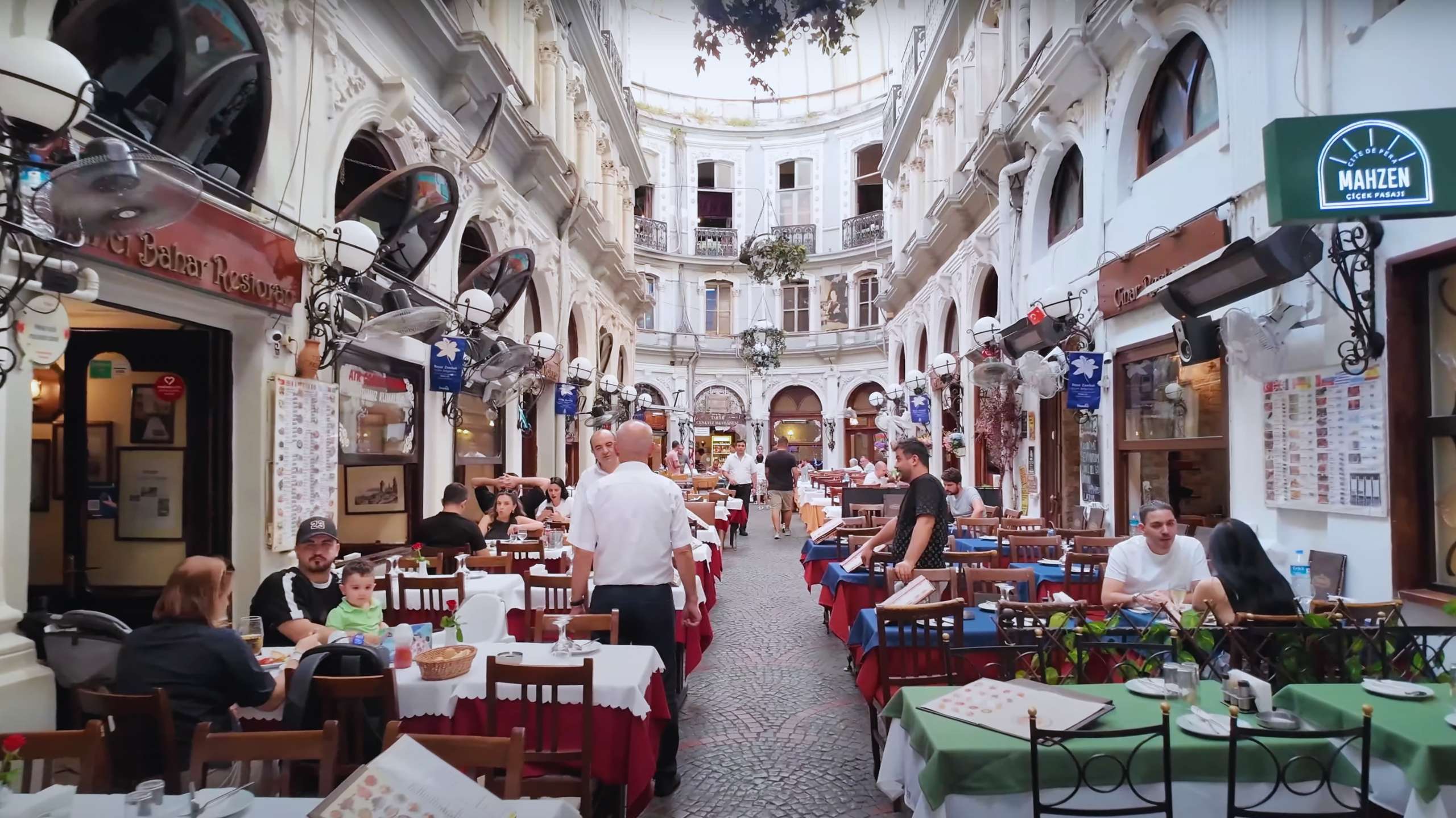 Cozy seating under a grand, historic arcade where locals and tourists enjoy Turkish cuisine.