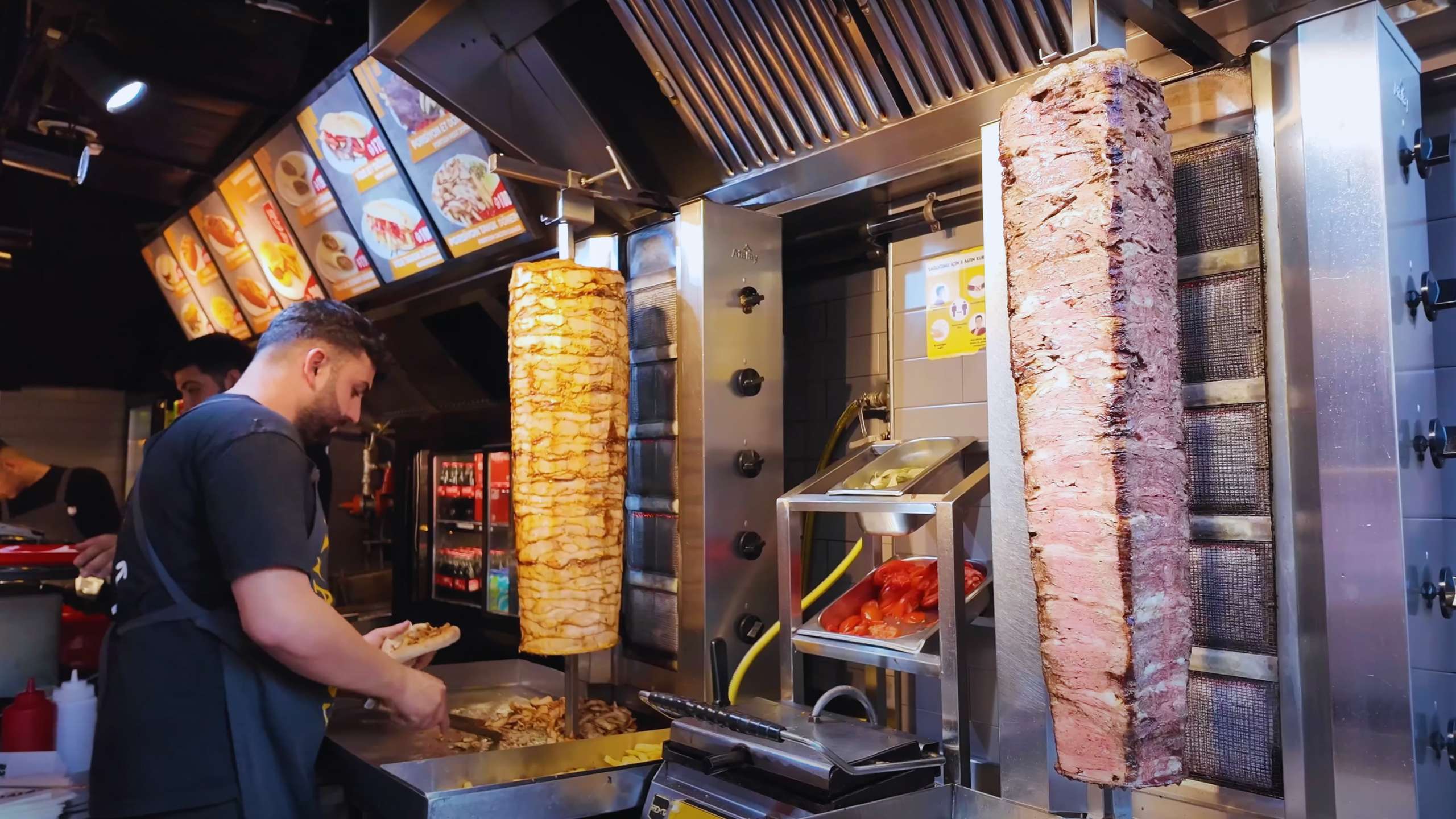 A chef slicing döner meat from large skewers in a bustling fast-food spot.