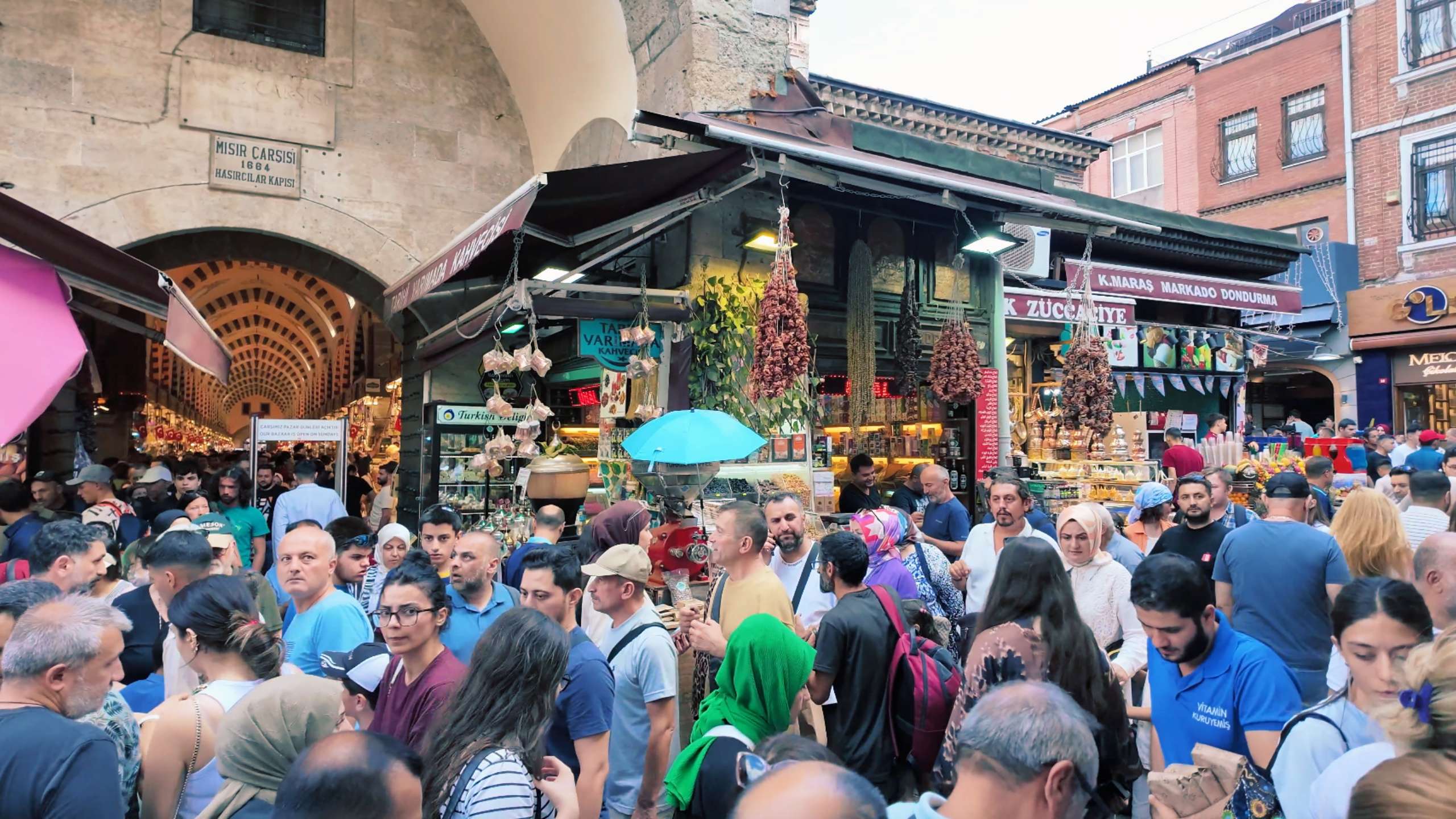 Crowds bustle through an archway, exploring market stalls filled with Turkish goods.