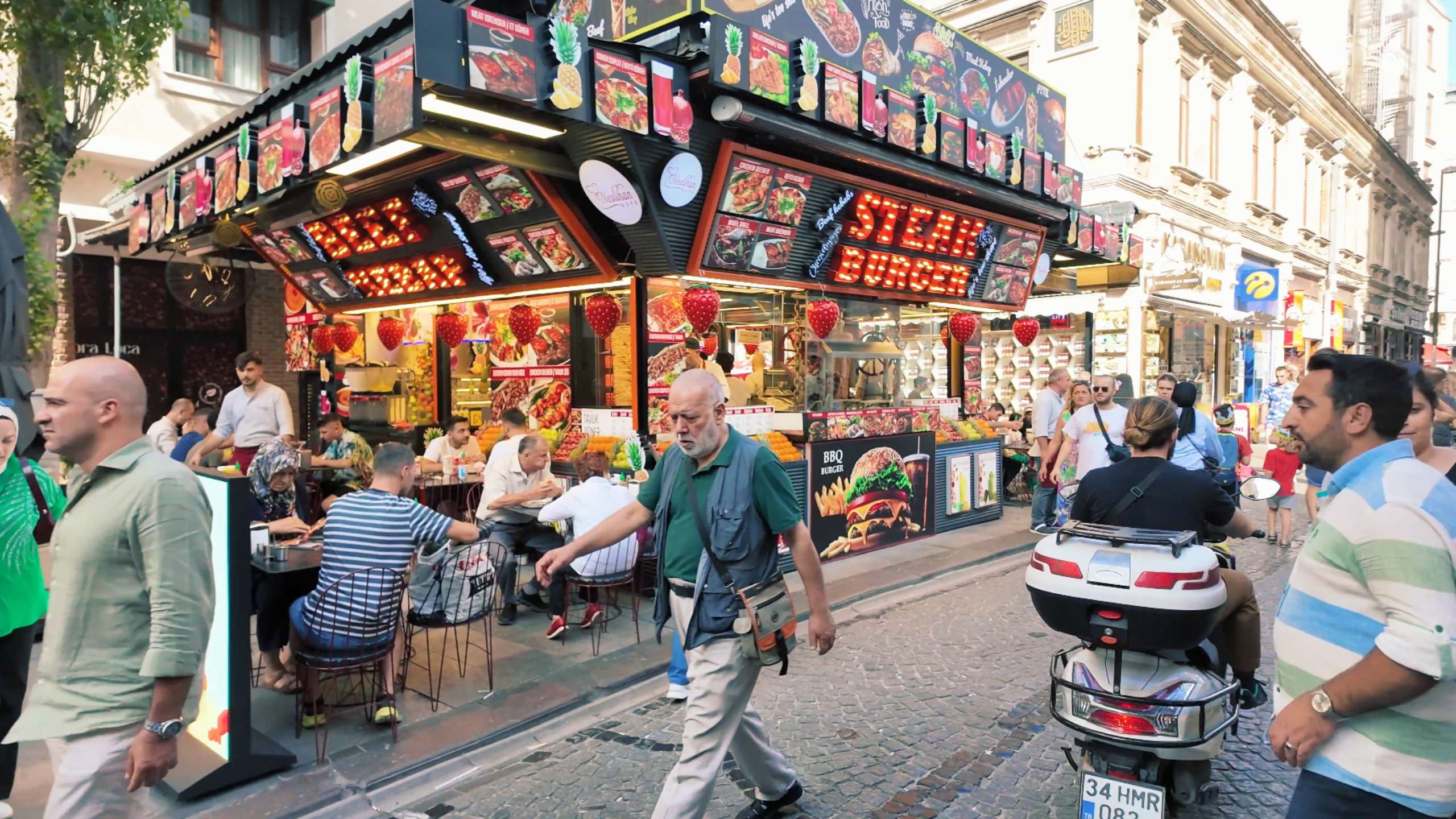 A bustling outdoor restaurant draws locals and tourists with its vibrant signs and street food.