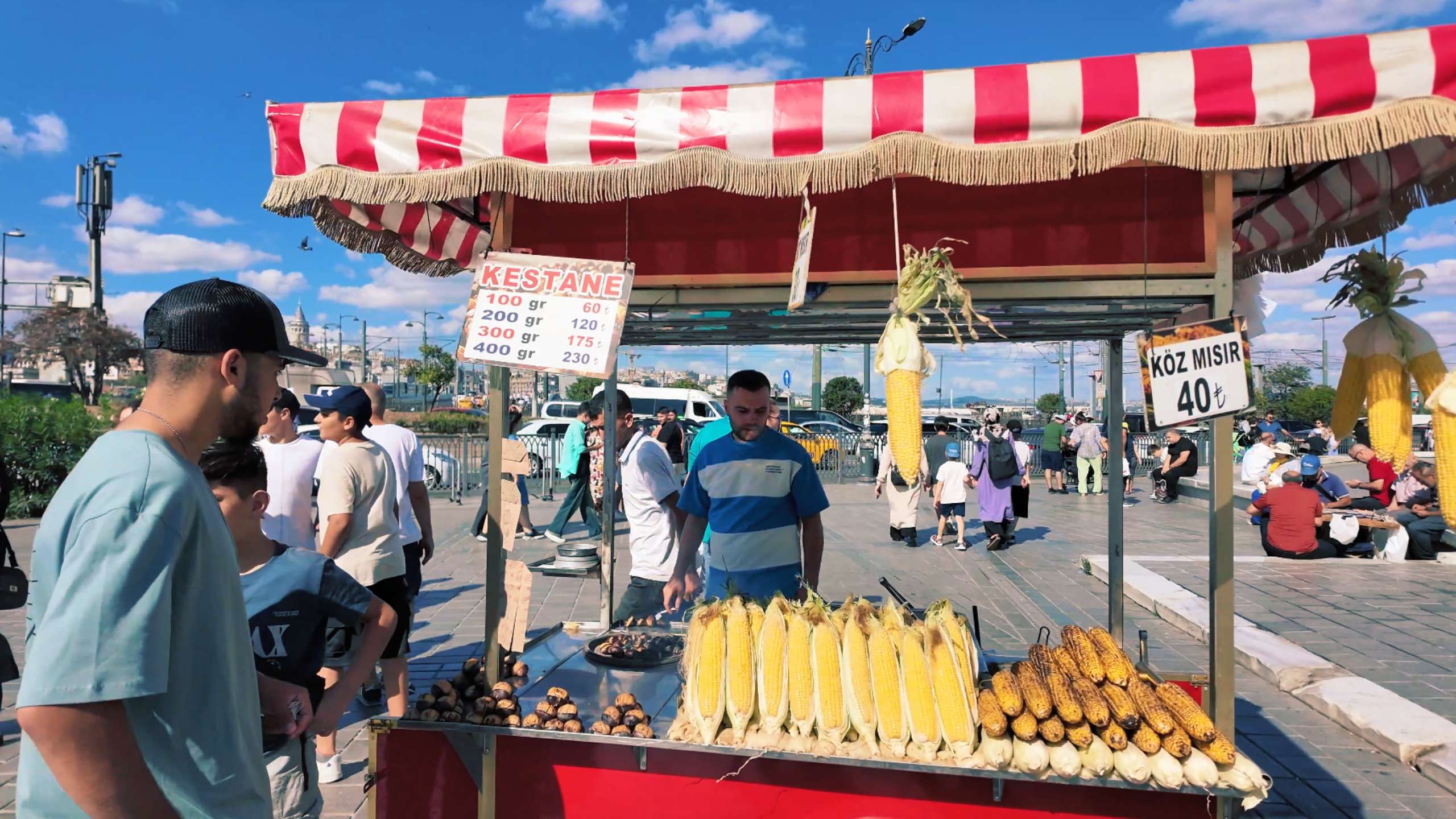 A street vendor sells roasted corn and chestnuts under a red-striped canopy.