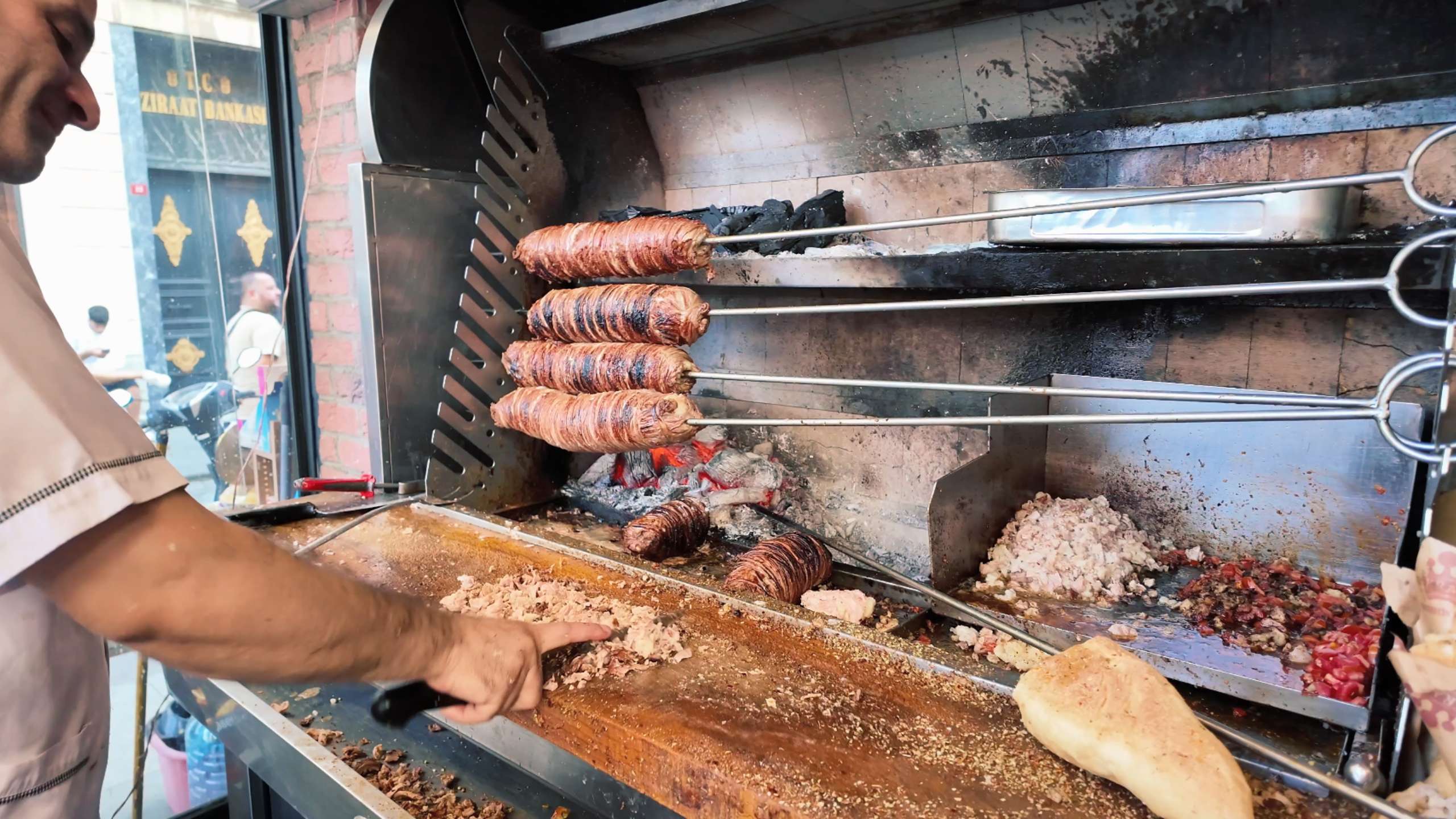 A chef skillfully prepares kokoreç on skewers over a charcoal grill.