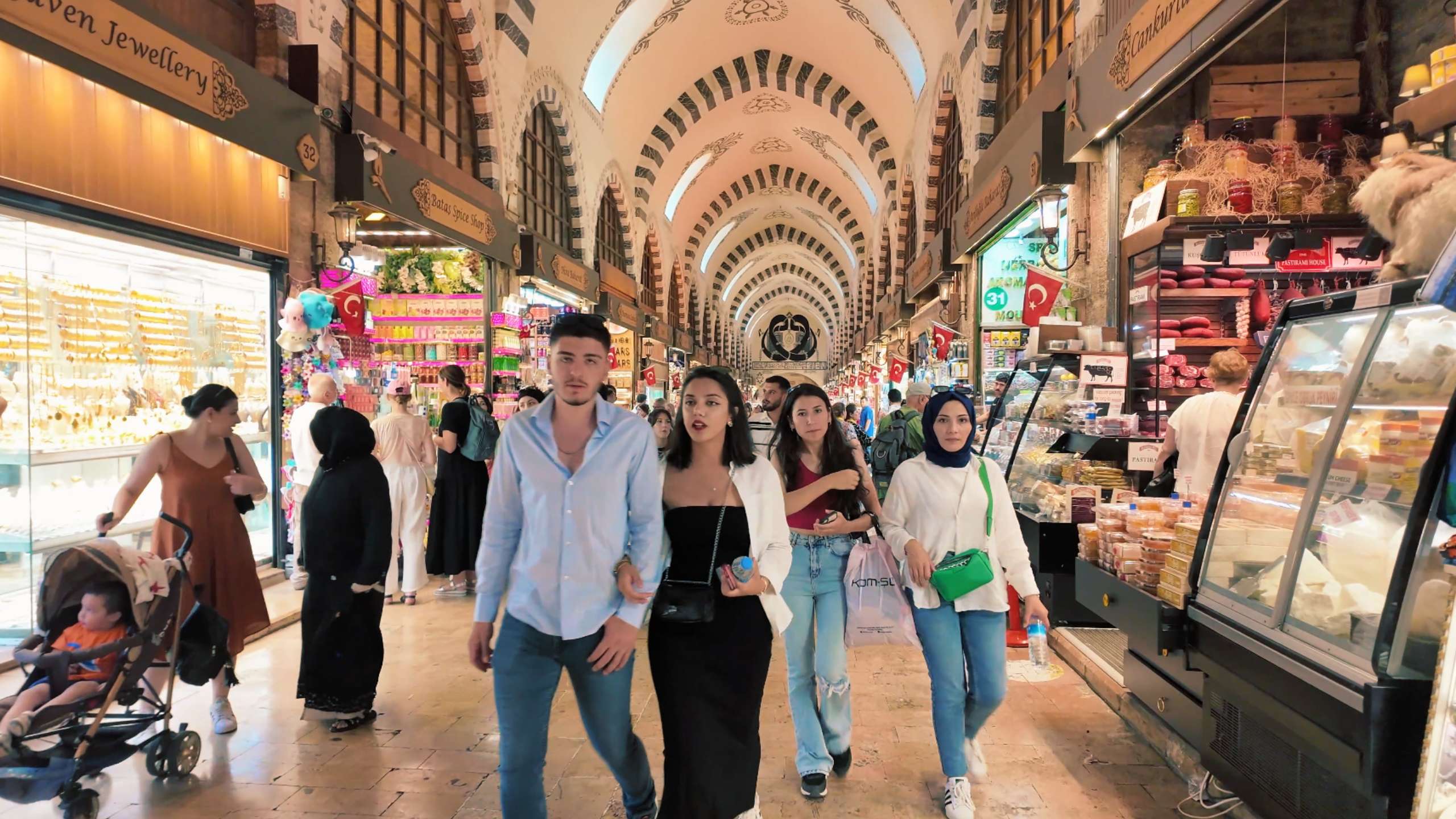 Visitors stroll under ornate, arched ceilings, surrounded by colorful shops and products.