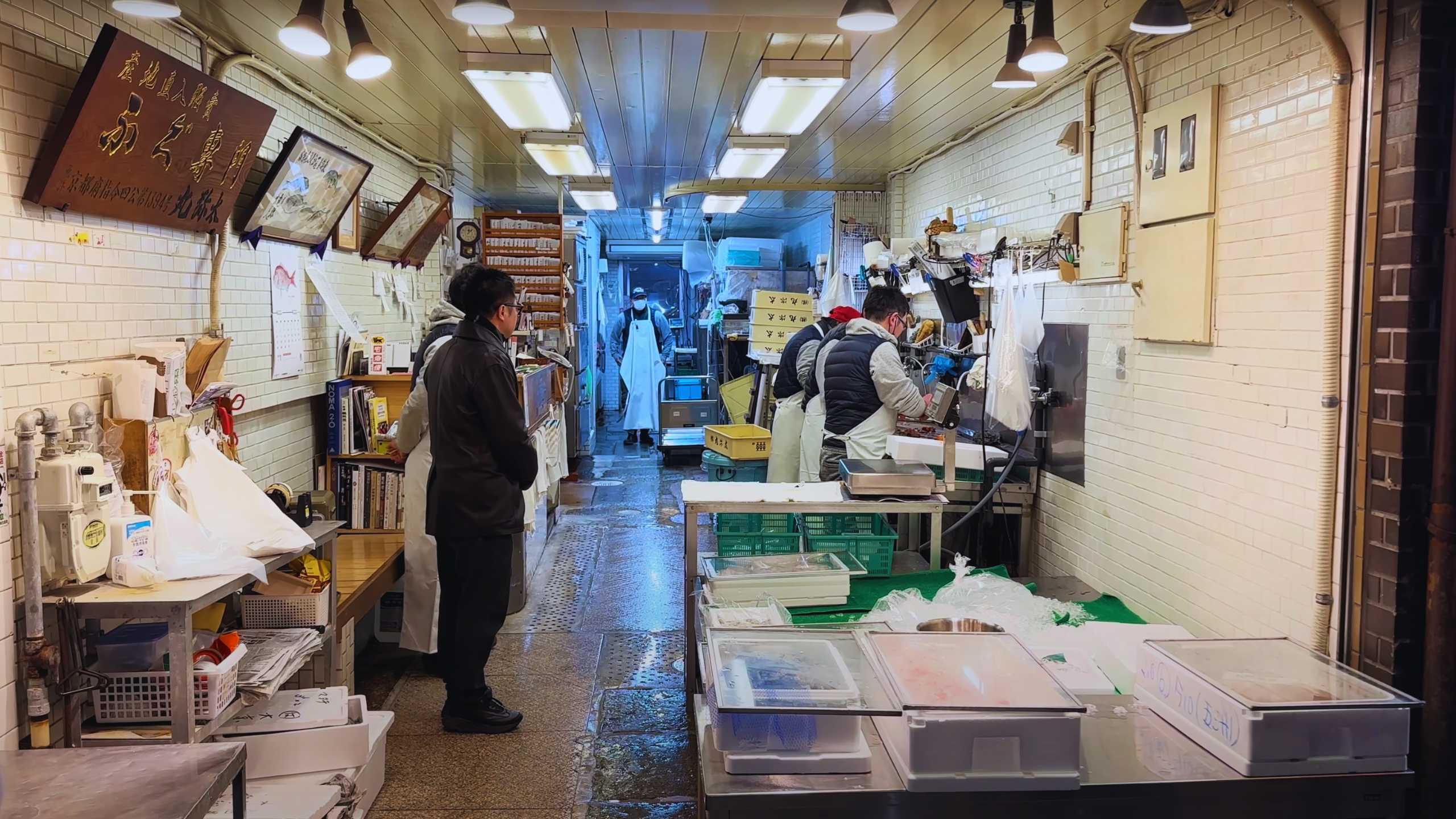 Workers processing seafood in a bustling Nishiki Market shop.