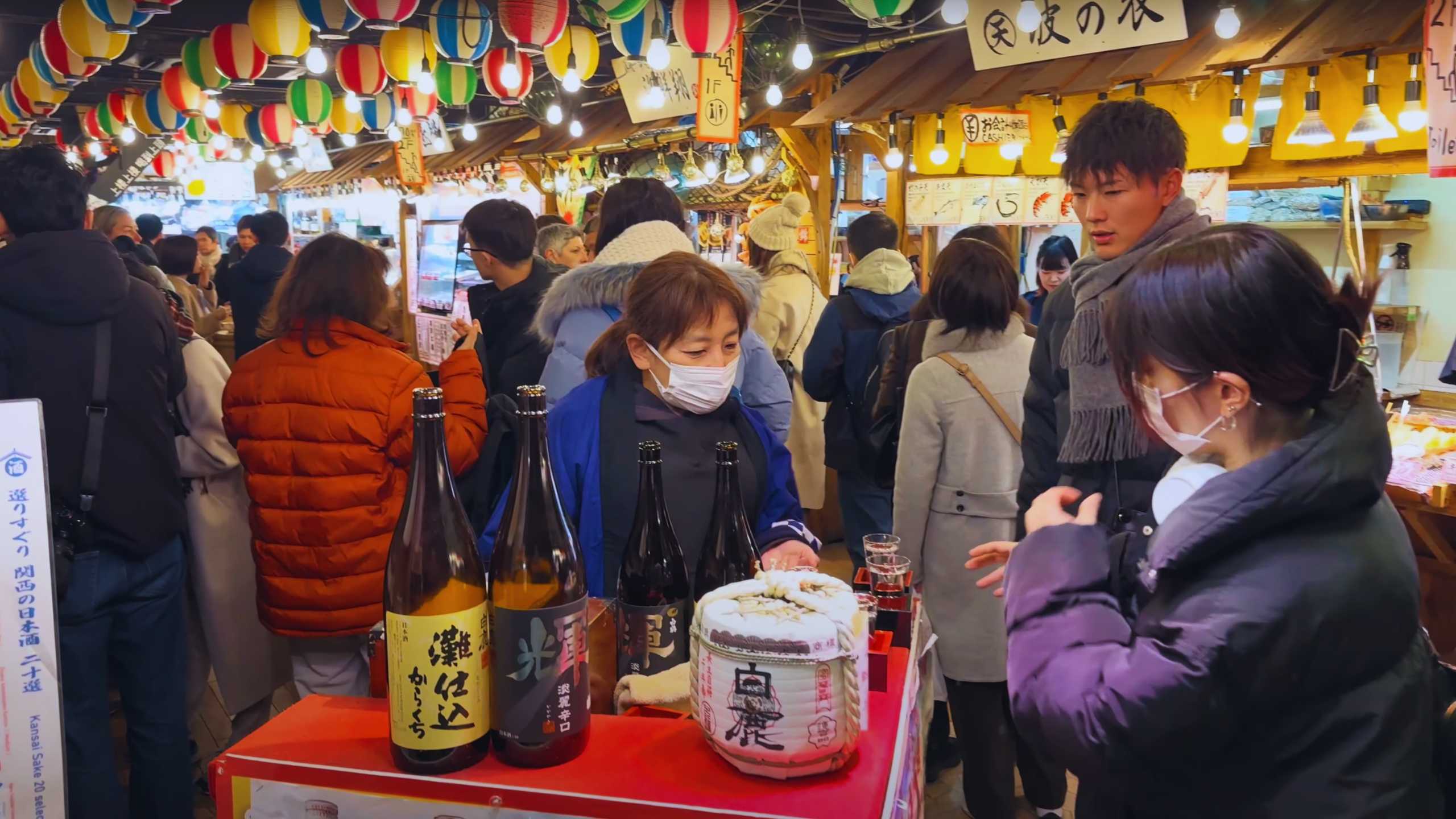 Visitors explore a bustling market stall offering a variety of sake.