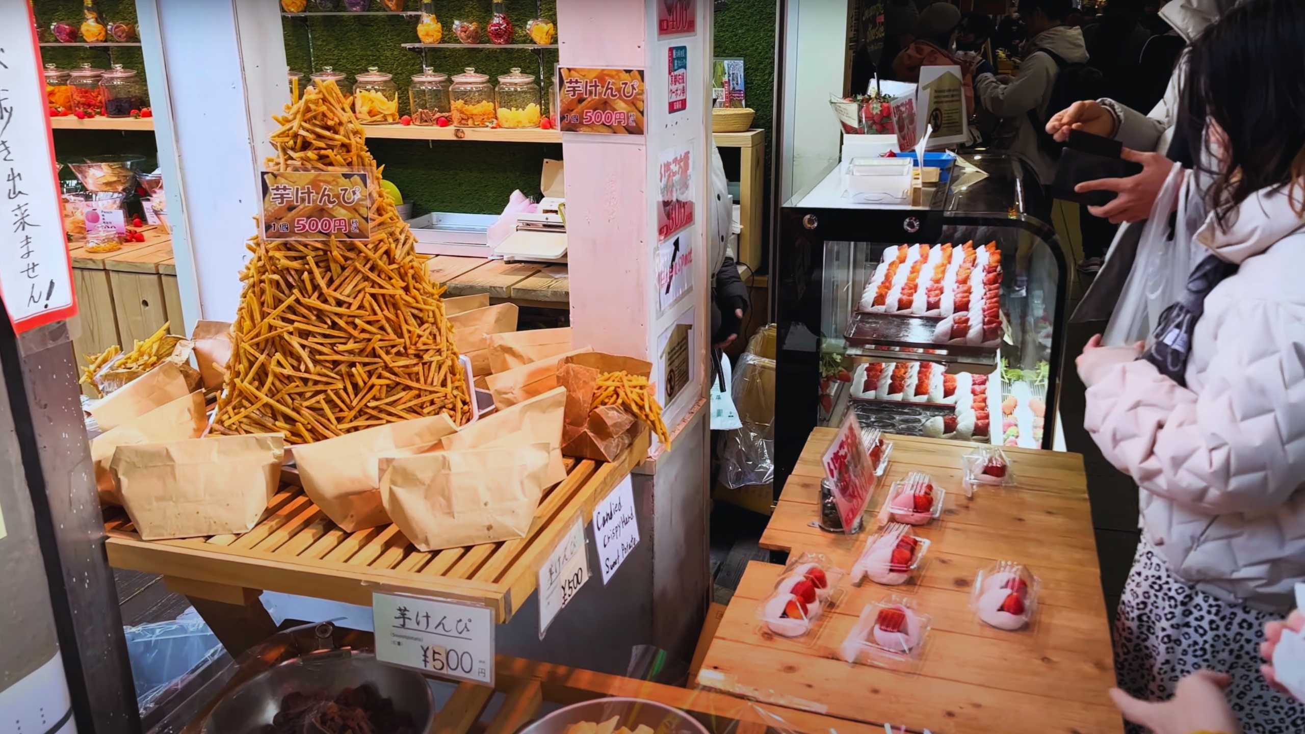 Display of sweet potato sticks and strawberry desserts at a market stall.