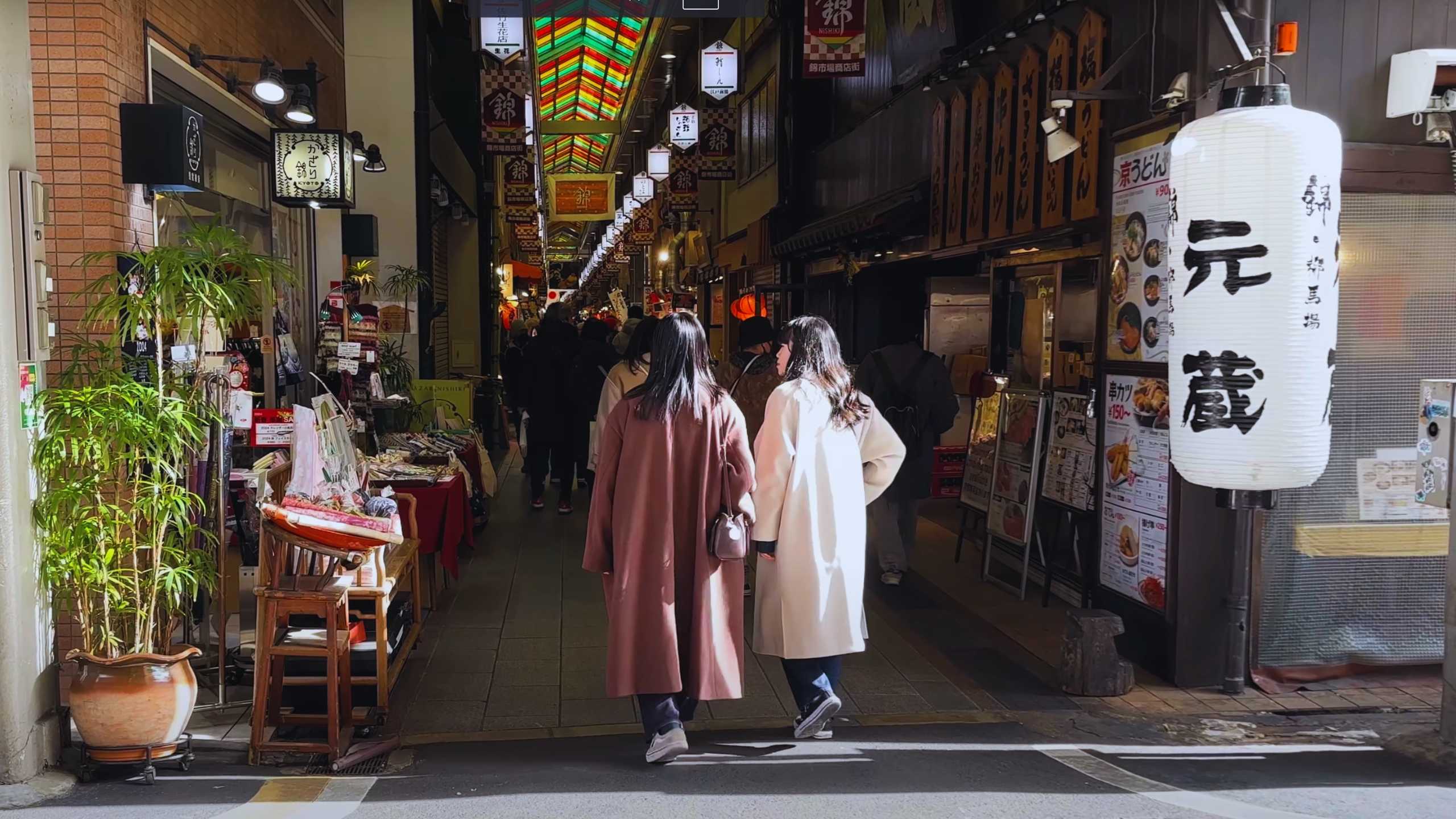 Shoppers walking through a colorful, lantern-lit Japanese market street.