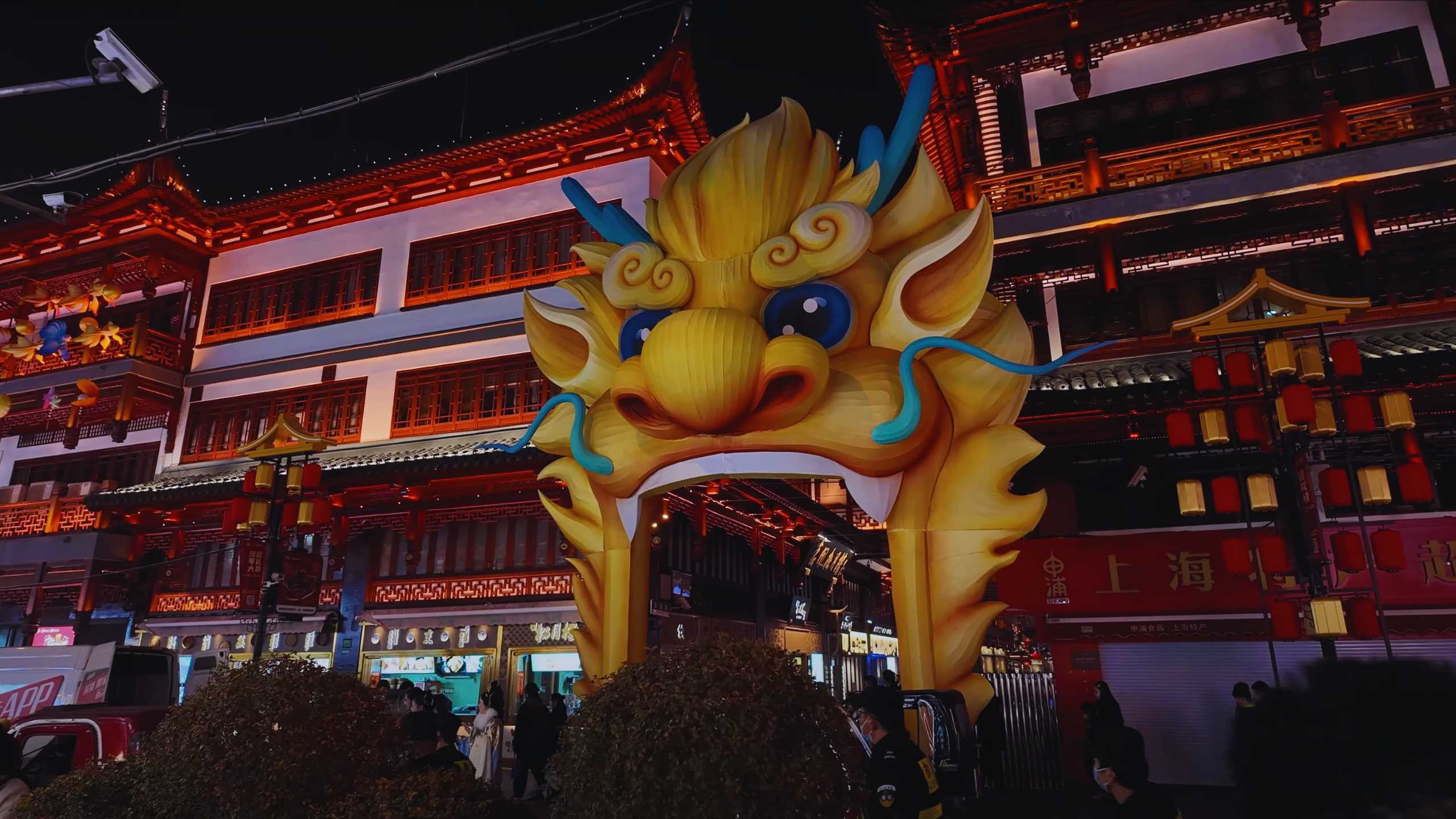 Brightly lit dragon head decoration against traditional red buildings.