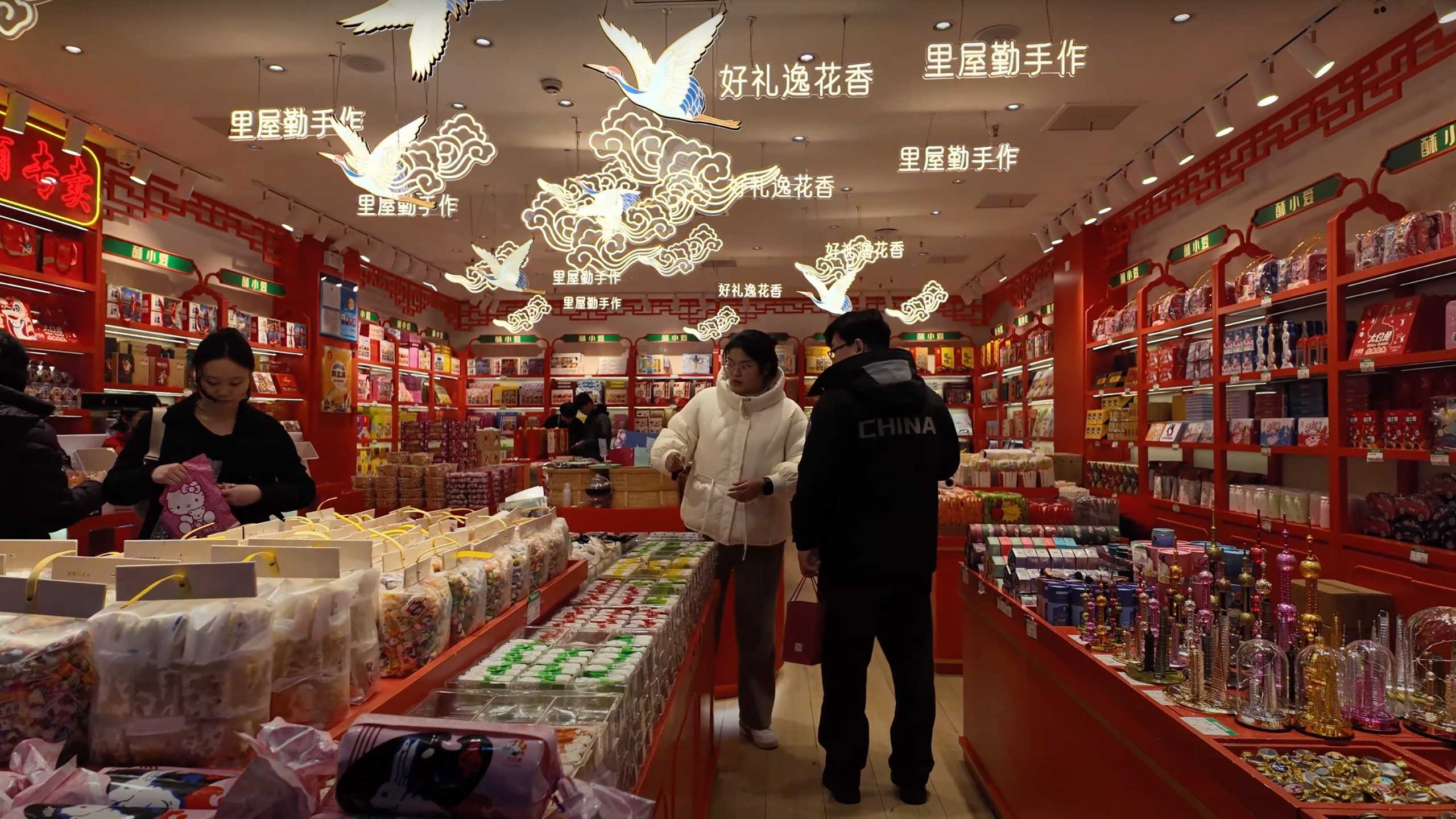 Shoppers browsing in a warmly lit, red-themed souvenir store.