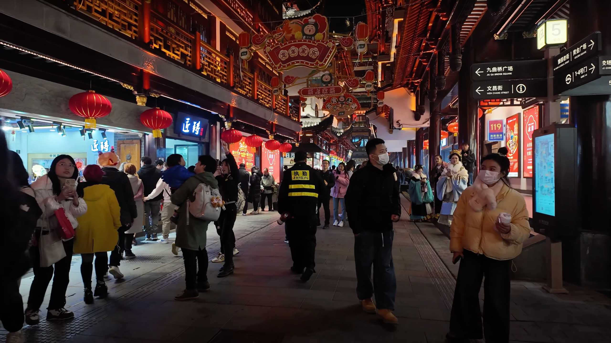 Crowds strolling beneath red lanterns in a bustling, decorated street.