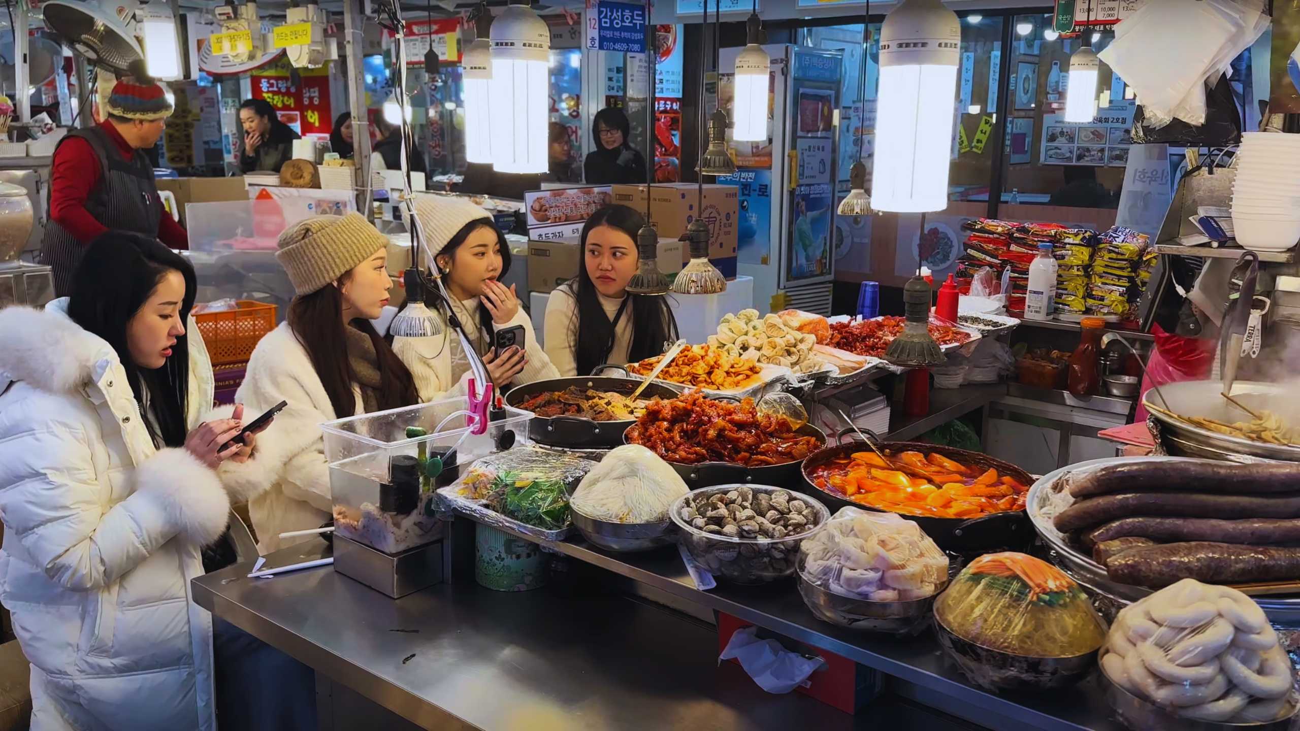 Four friends seated at a busy food stall, sharing a meal and conversation.