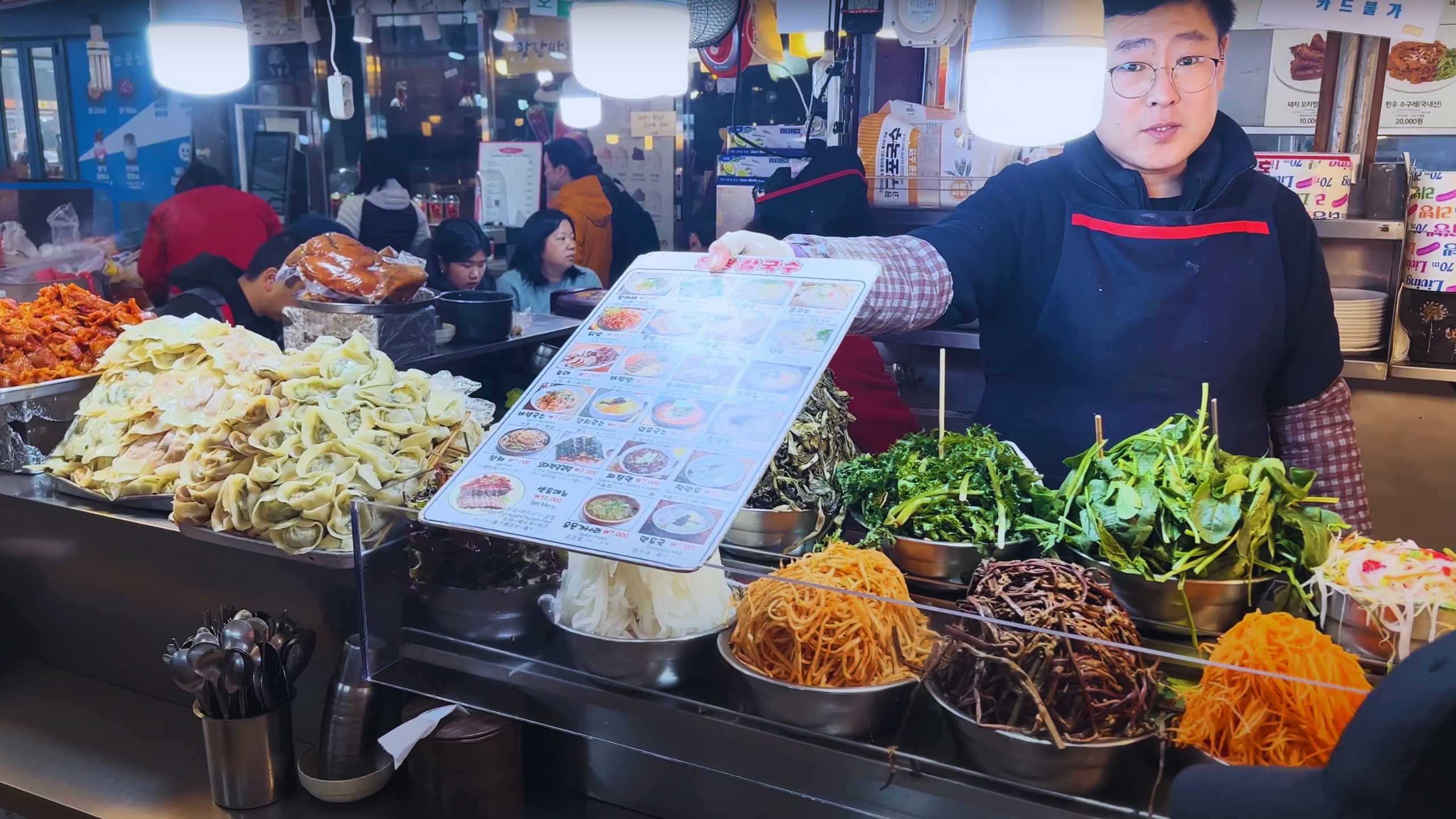 A vendor proudly holding up a menu, surrounded by fresh greens and a variety of colorful ingredients.