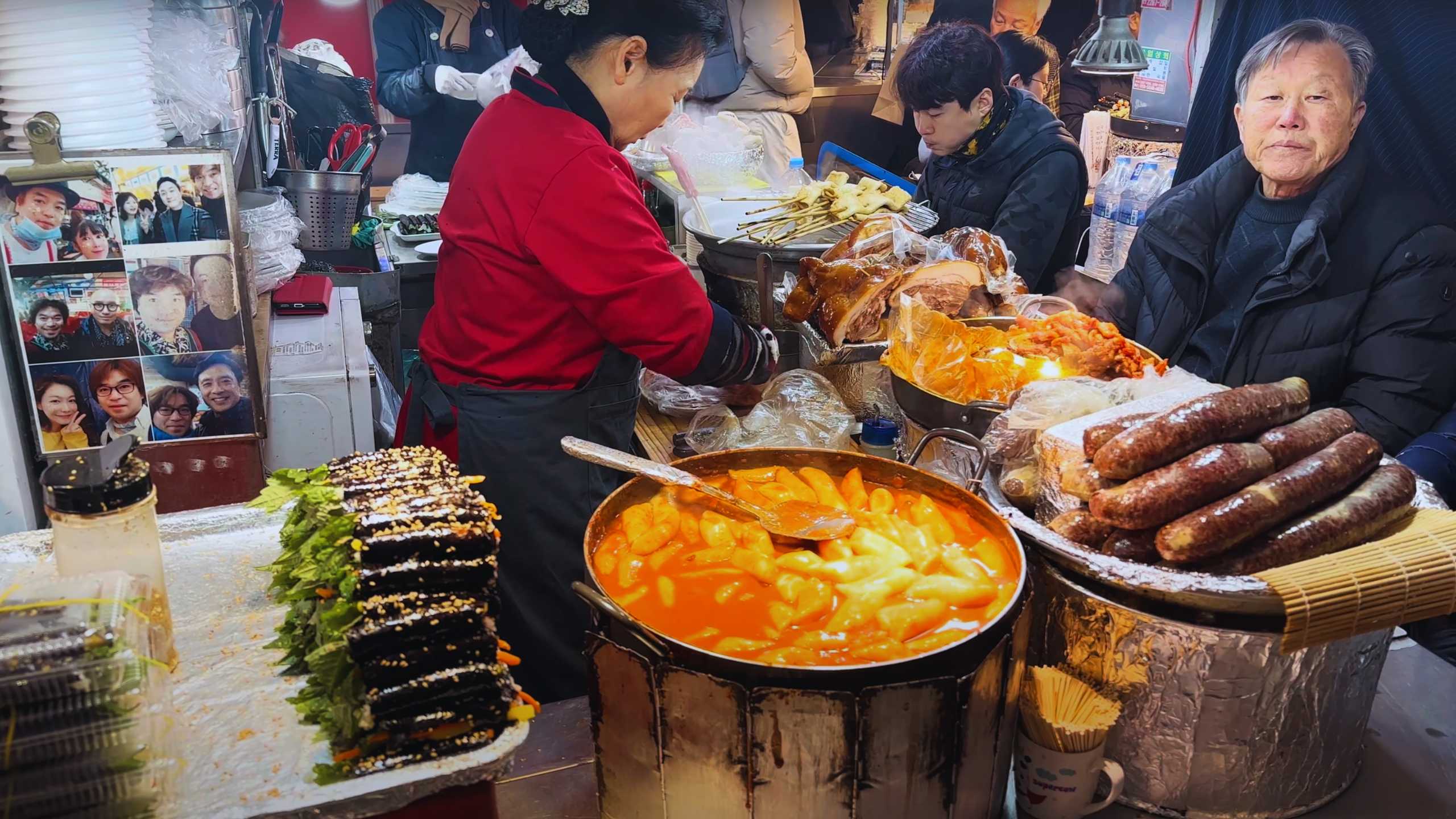 A steaming pot of tteokbokki front and center, surrounded by stacks of freshly made gimbap and sausages.