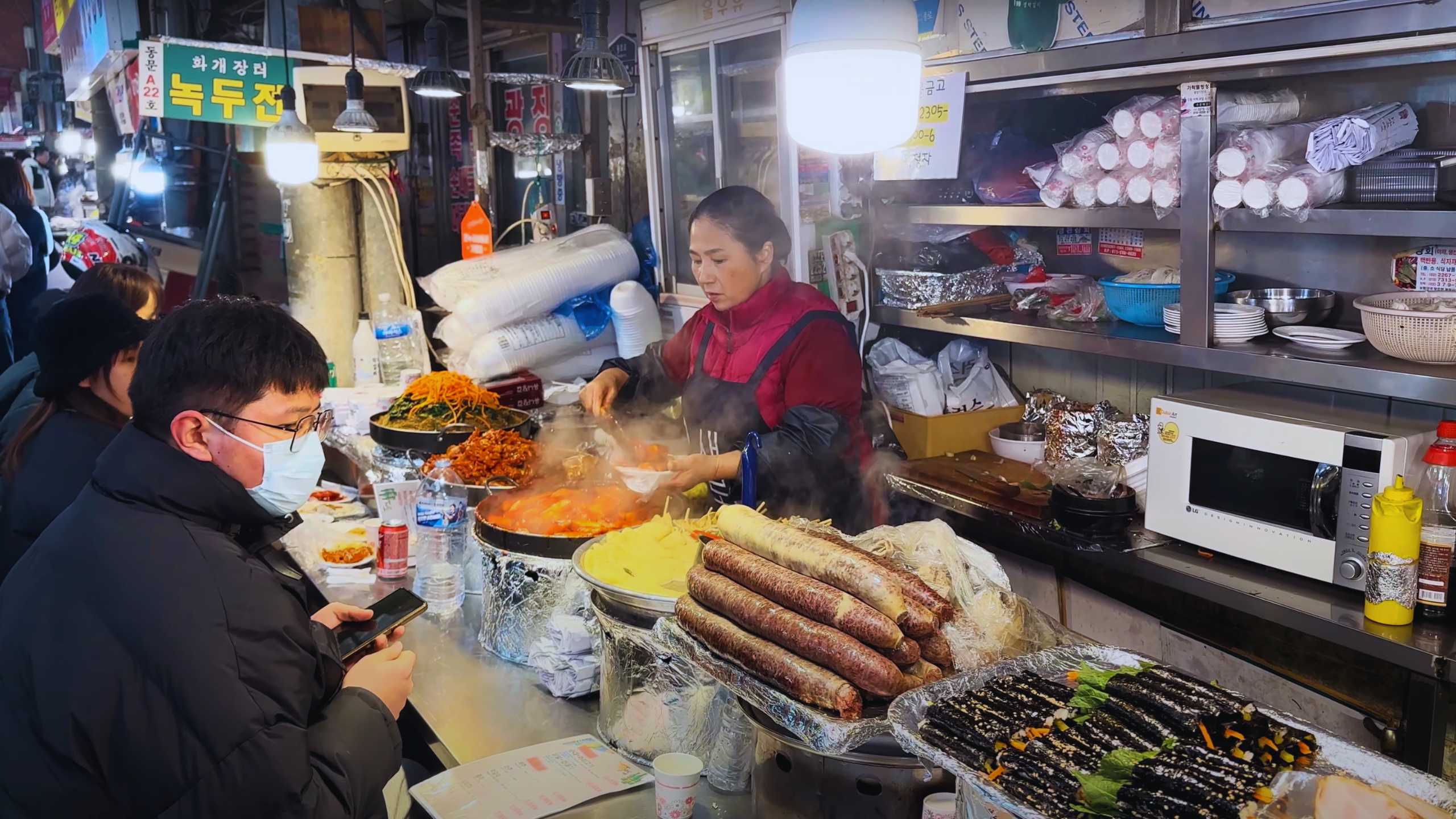 A vendor serving up hot food to customers, with steaming pots and fresh ingredients in view.