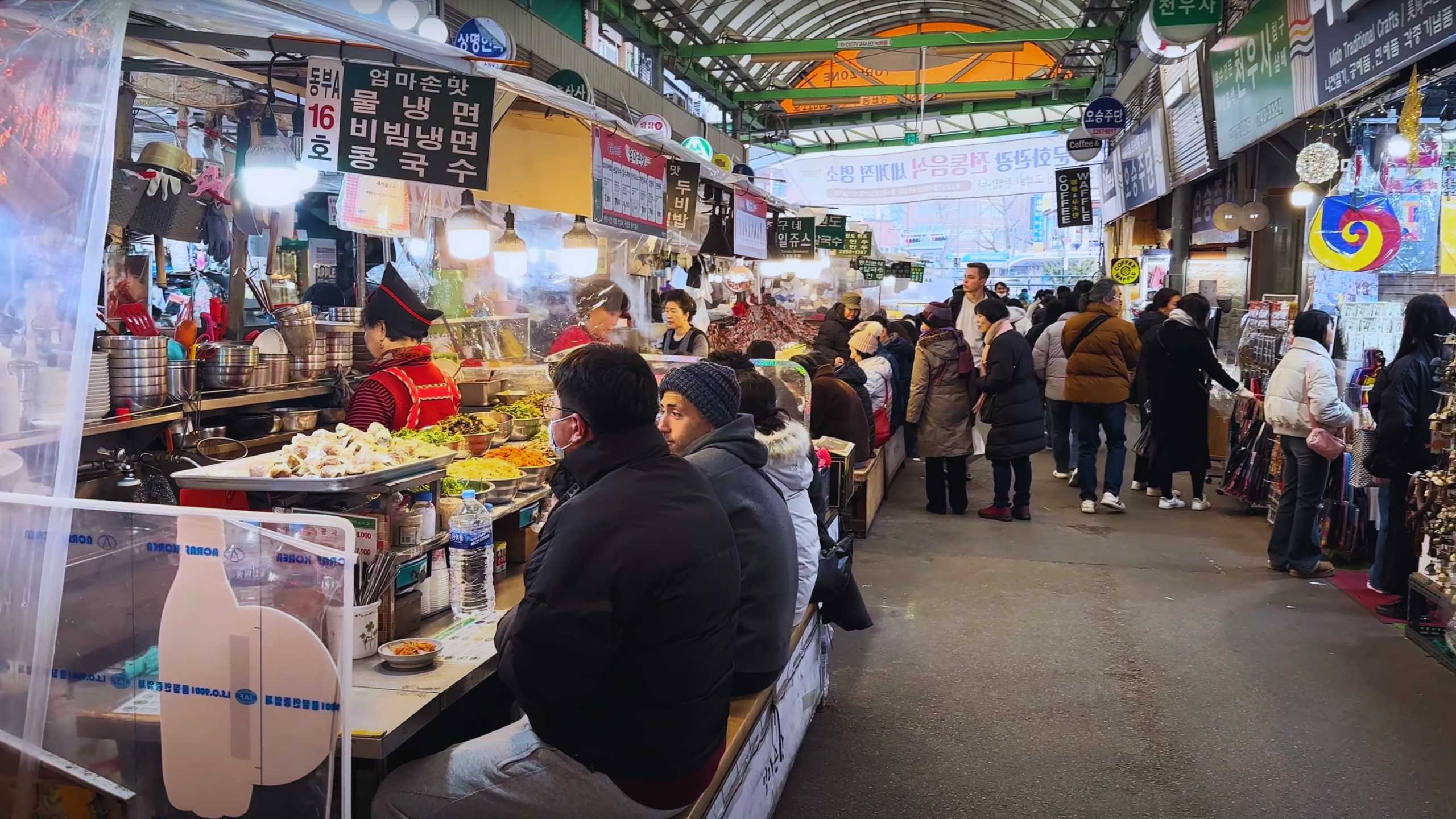 Market patrons enjoy traditional Korean dishes amidst the bustling atmosphere.