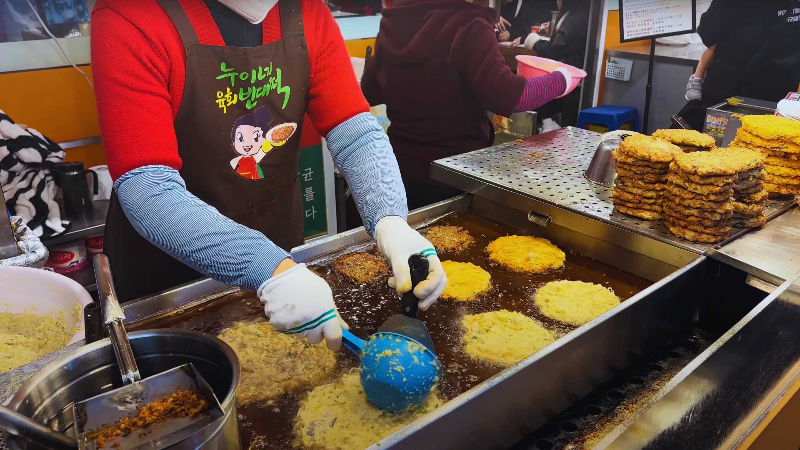 A vendor frying savory pancakes, golden brown and crispy, as they float in hot oil.