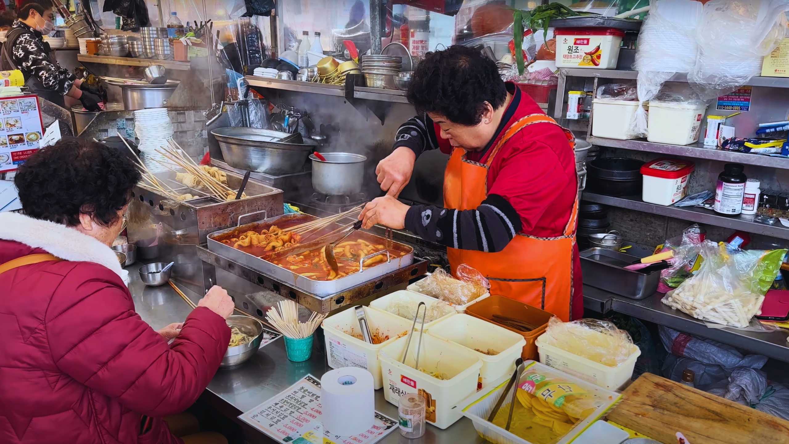 A vendor skillfully prepares spicy tteokbokki for a waiting customer.