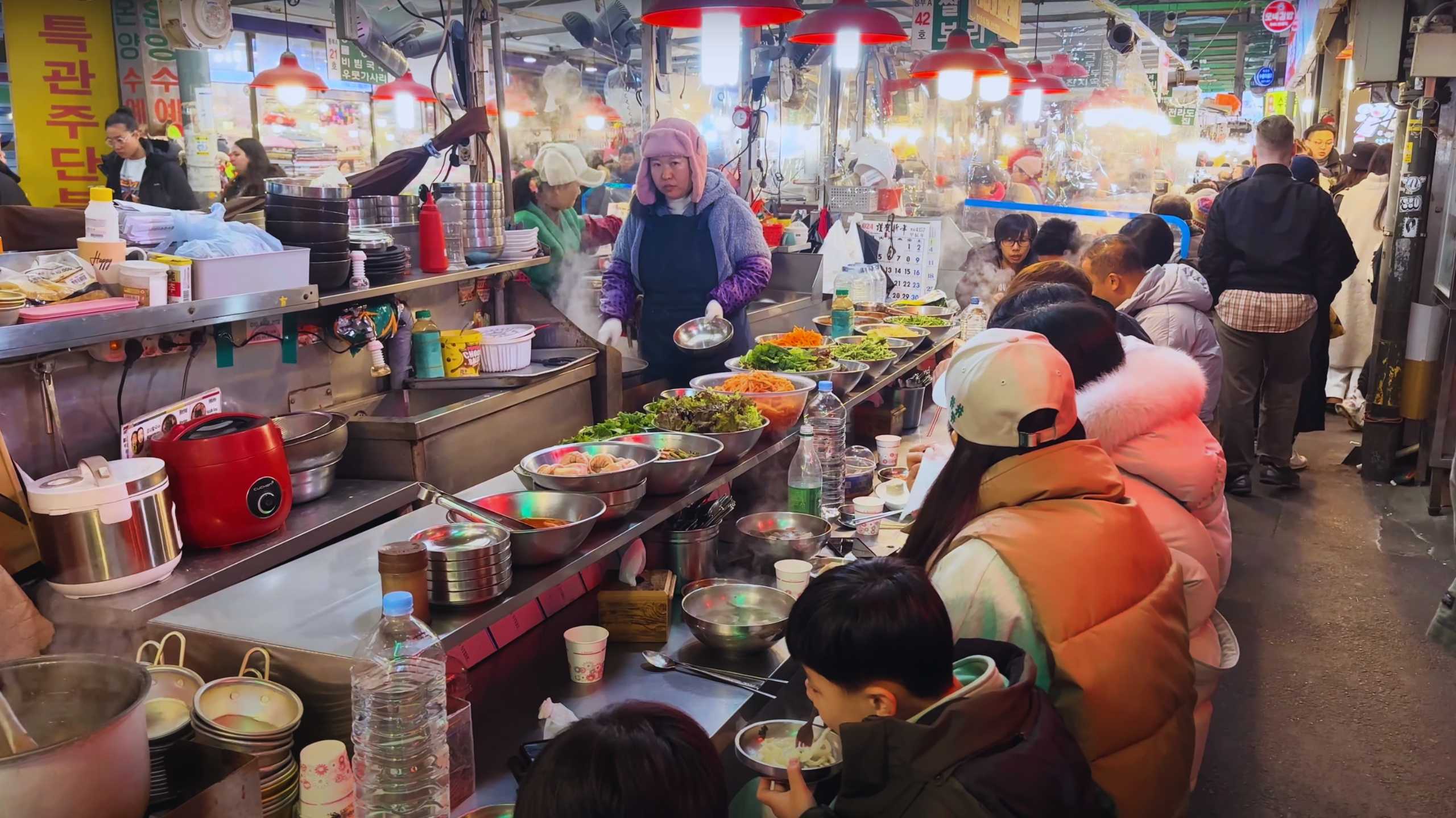 A row of patrons seated at a bustling food stall, enjoying hot soups and noodles.