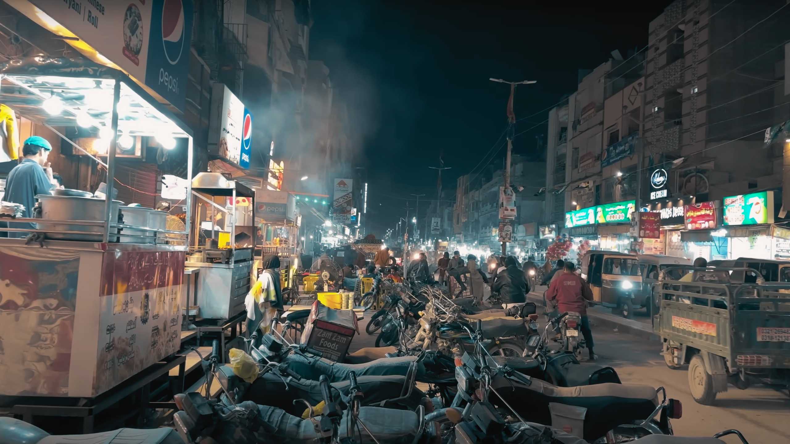 A bustling night scene filled with vibrant food stalls and motorcycles.