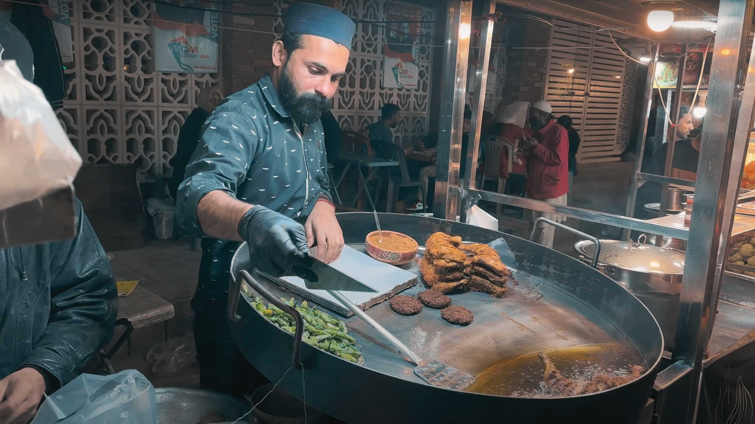 A vendor focuses on grilling spicy kebabs as the market buzzes with energy.