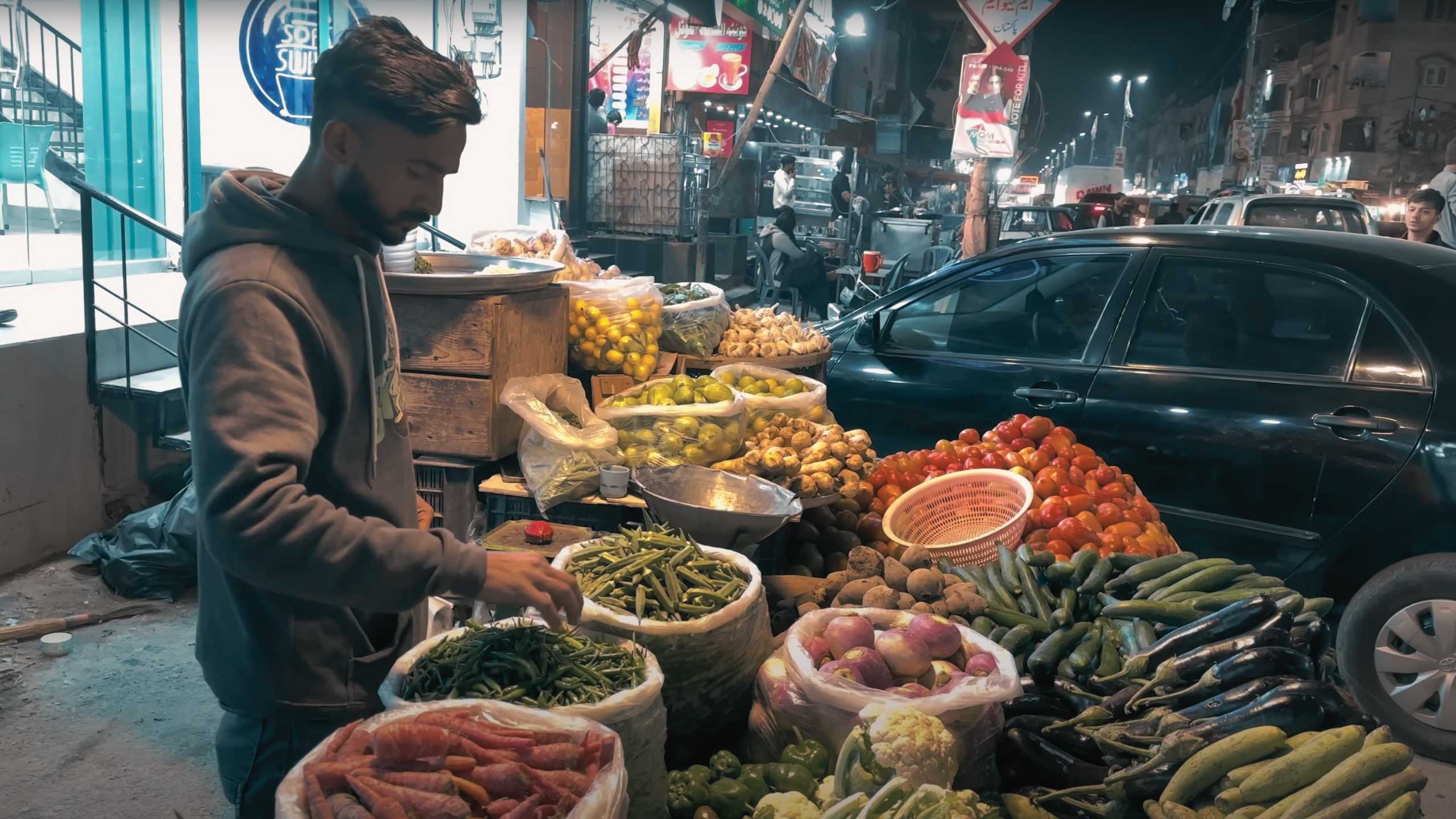 A vendor carefully stack fresh produce under the streetlights.