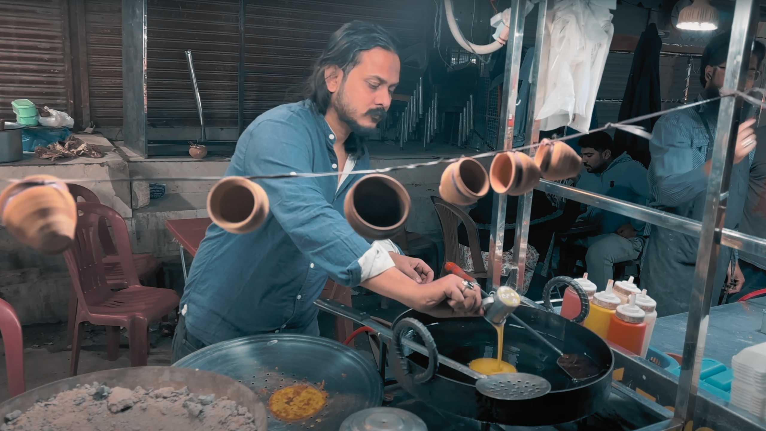 A man meticulously crafting a traditional dish with clay cups hanging nearby, capturing tradition in modern times.