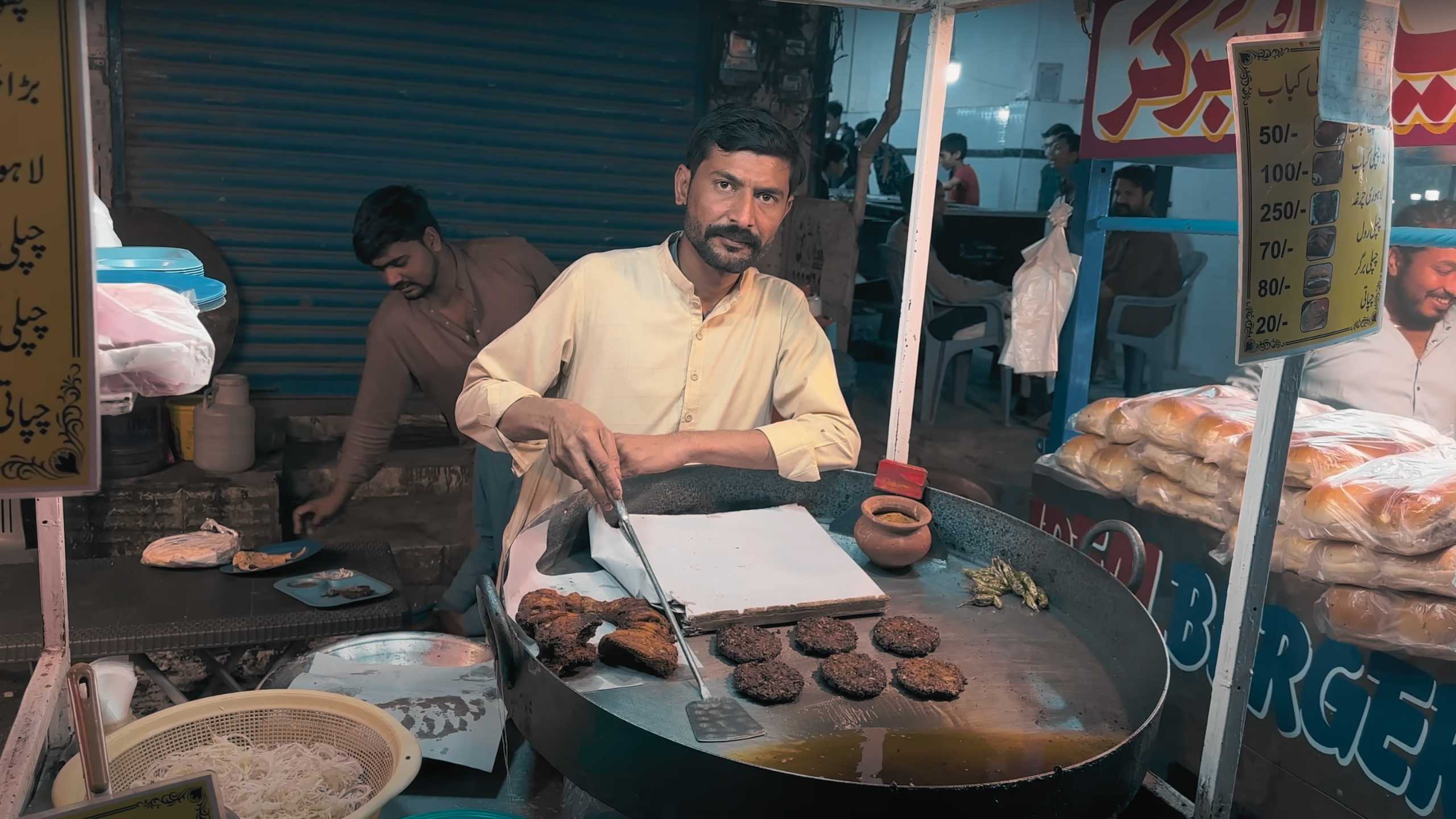 A vendor grilling spicy kebabs, offering a warm smile to customers.