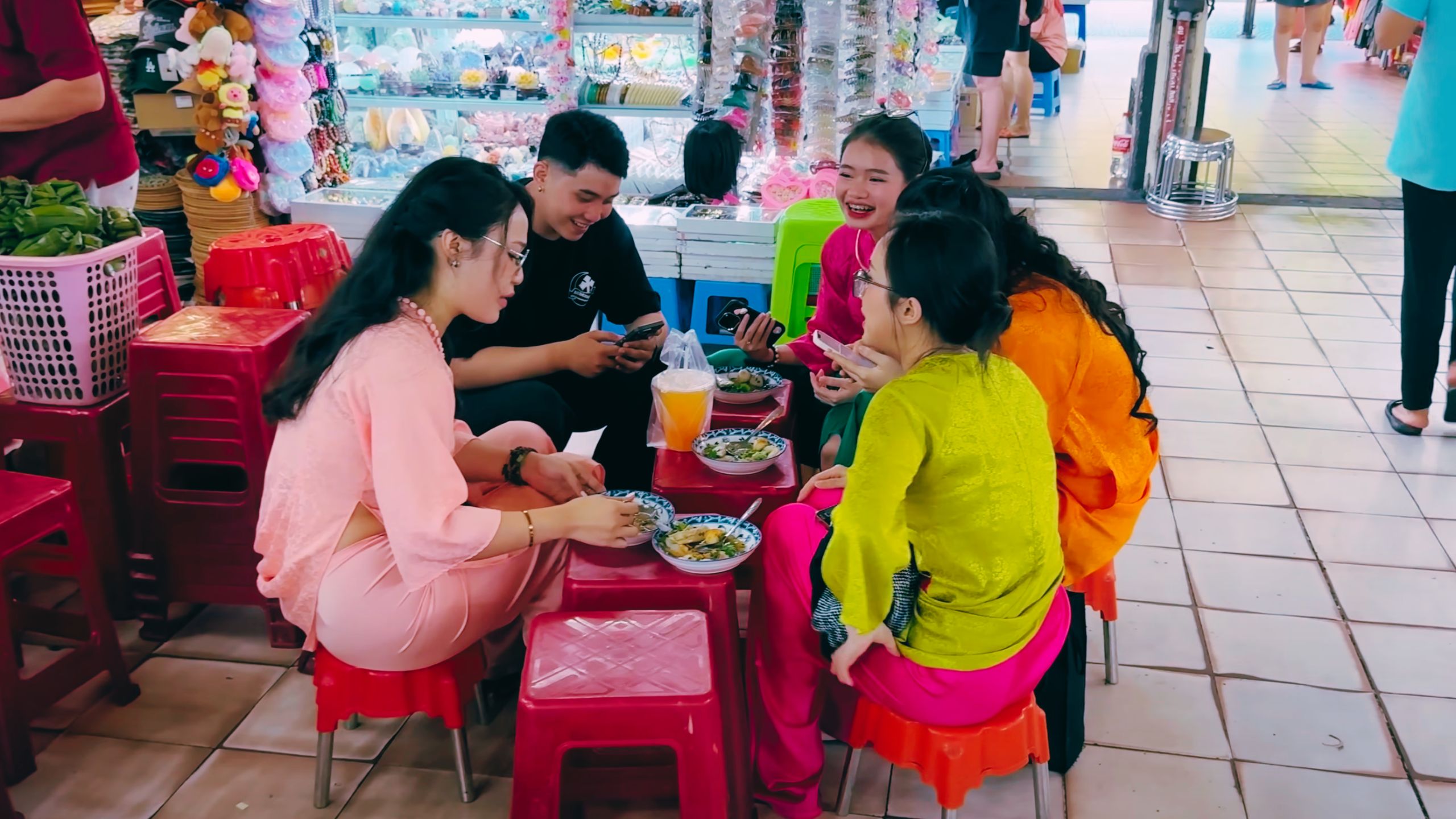A group of young Vietnamese friends enjoys street food and laughter on tiny stools.