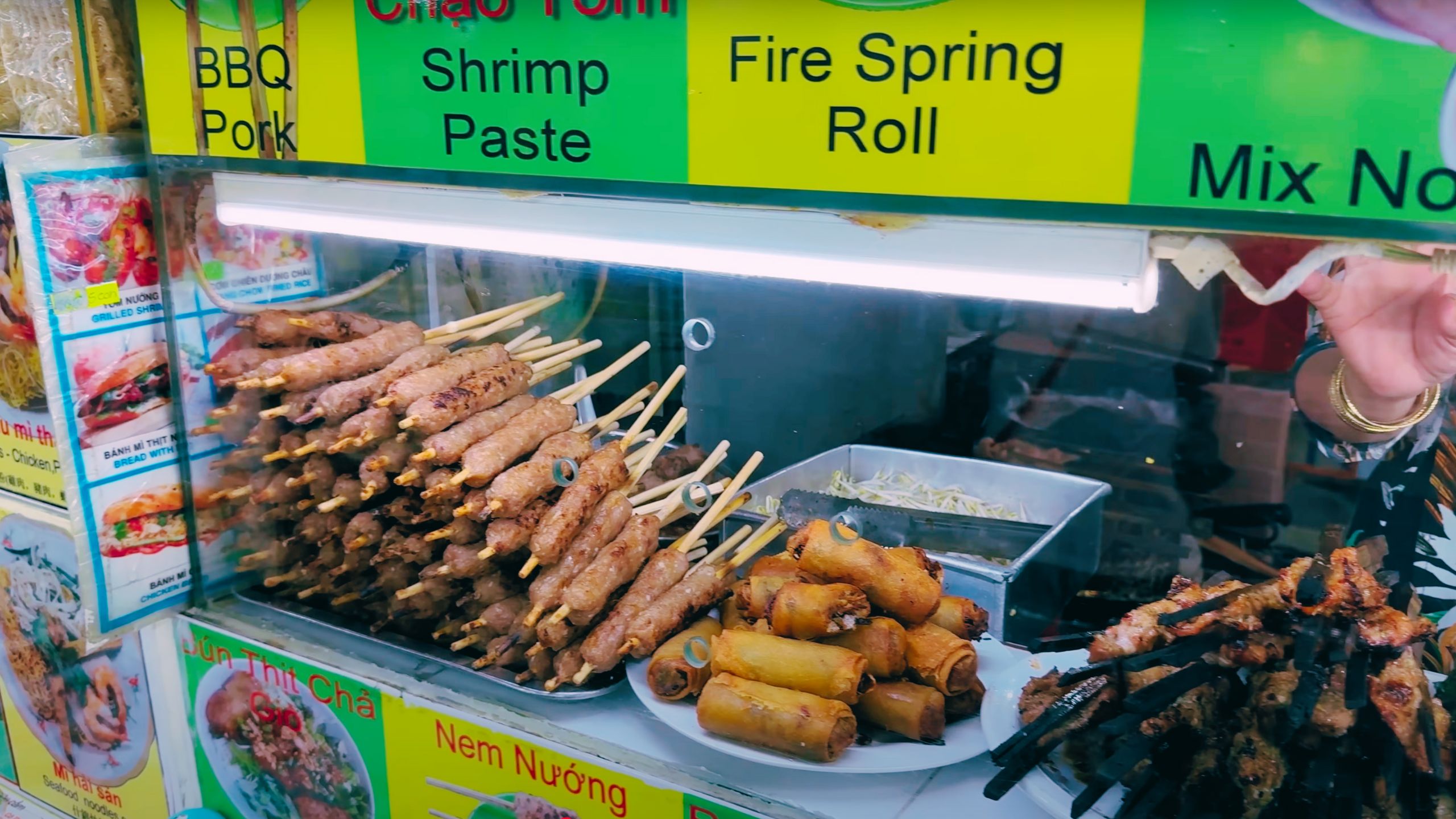 Skewered BBQ pork and crispy spring rolls displayed at a colorful food stall.