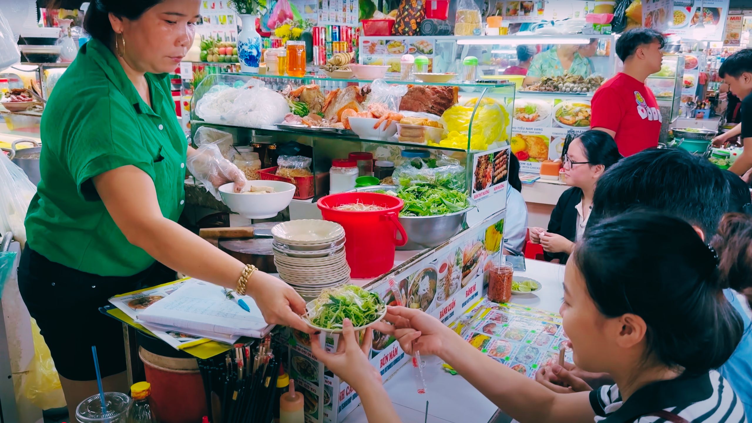 A vendor hands over a plate of freshly prepared greens and herbs at her stall.