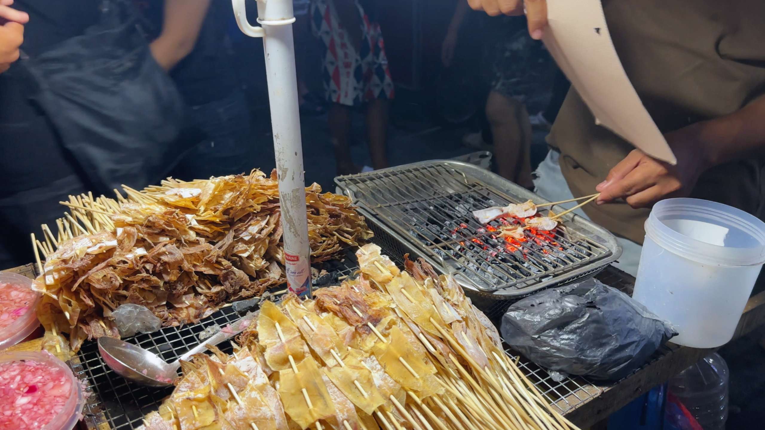 Vendor grilling skewers of dried squid over charcoal, filling the air with smoky aroma.