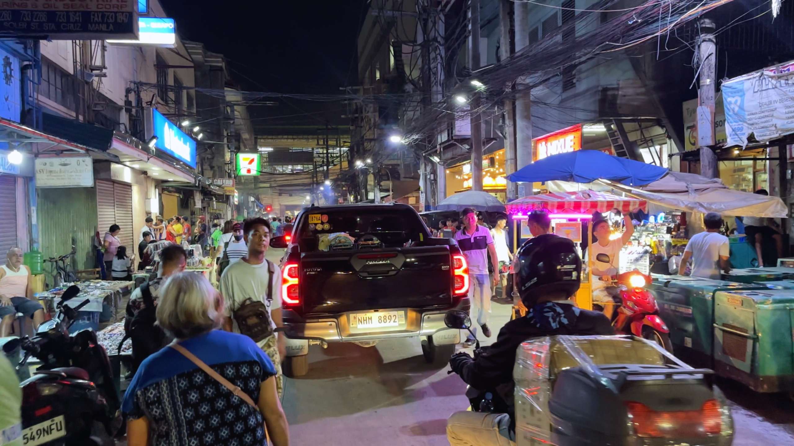 A bustling street scene filled with people, vendors, and vehicles navigating the vibrant night market.