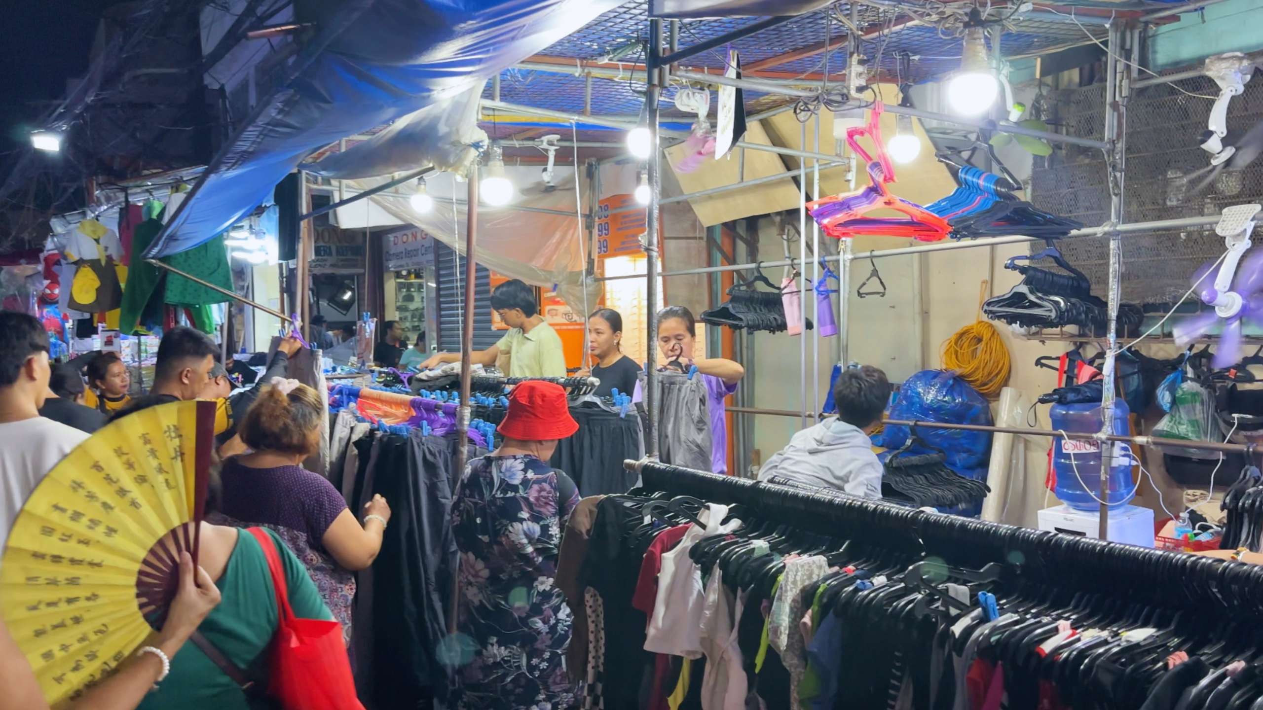 Shoppers browse through racks of colorful clothes under bright lights, adding to the market’s lively atmosphere.