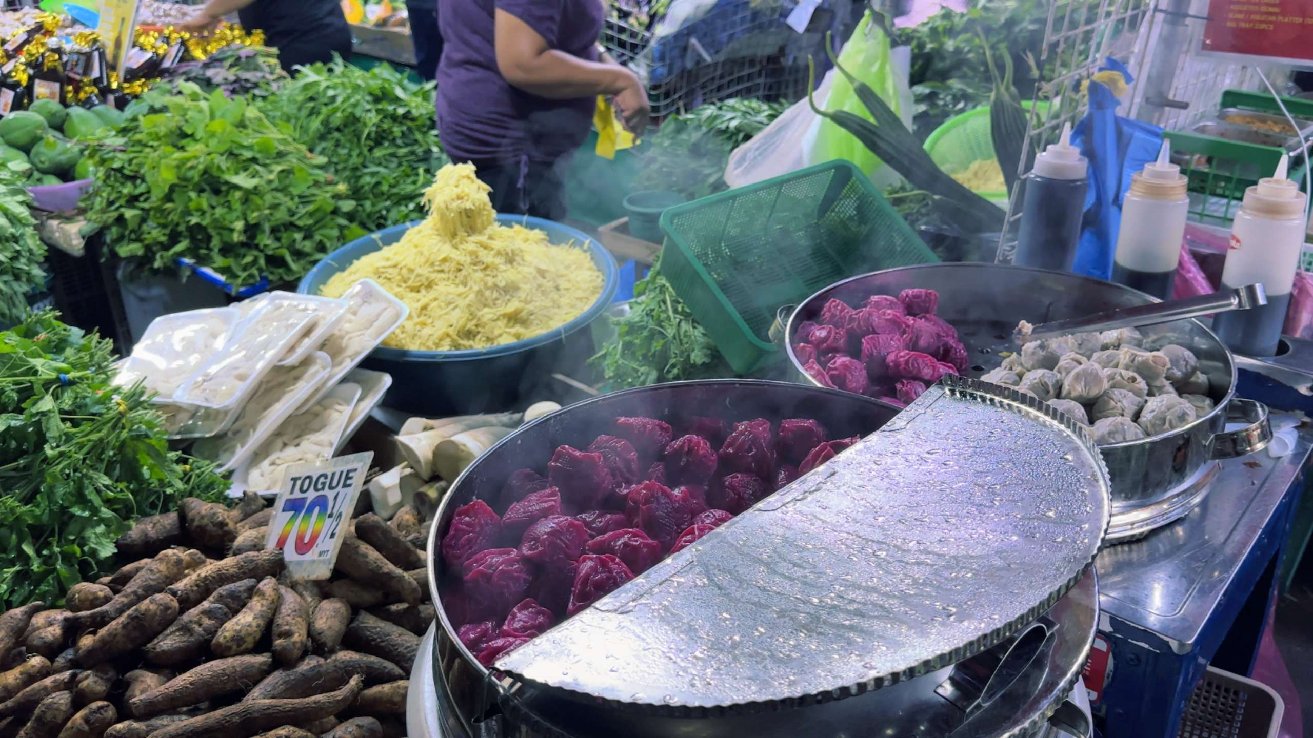 Brightly colored dumplings and fresh herbs steaming under market lights.