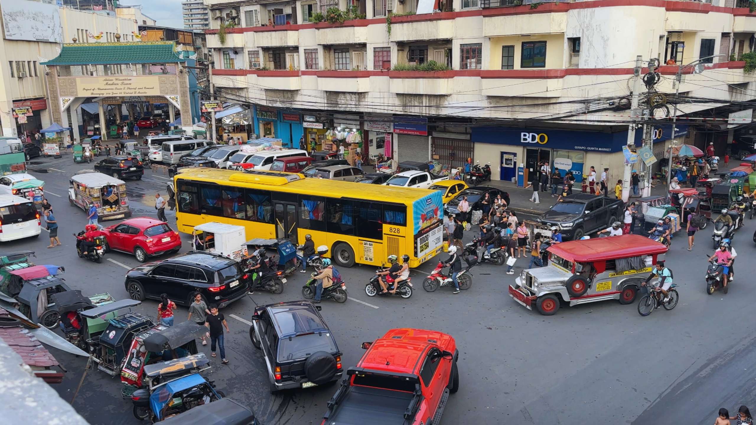 Bustling intersection filled with jeepneys, buses, and tricycles weaving through traffic.