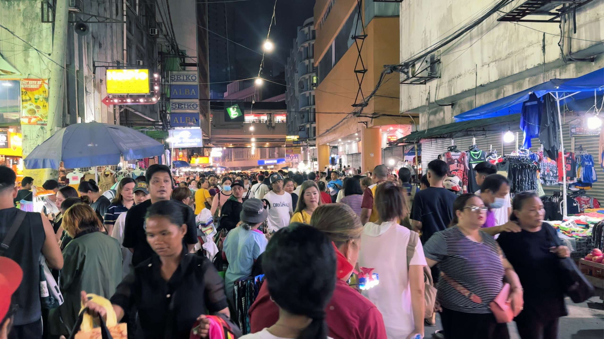 A dense crowd fills the market street, bustling with energy and activity.