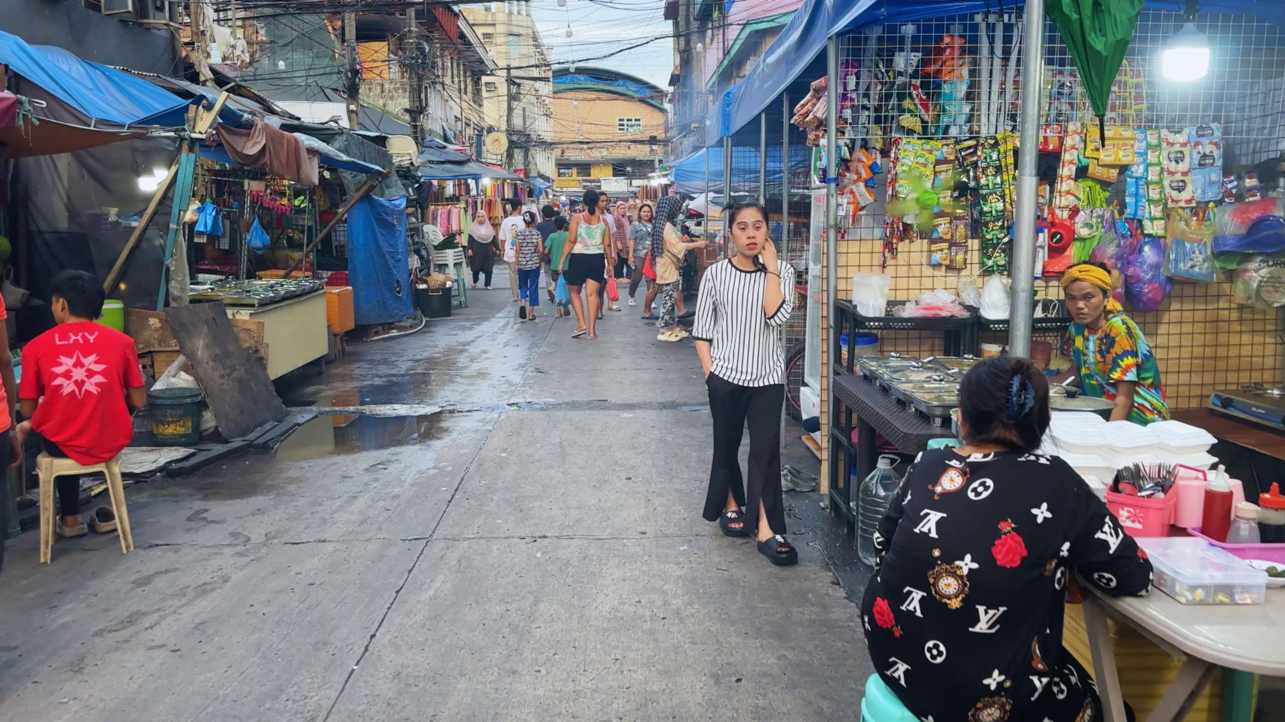 Narrow market alleyway with stalls and people walking among colorful displays.