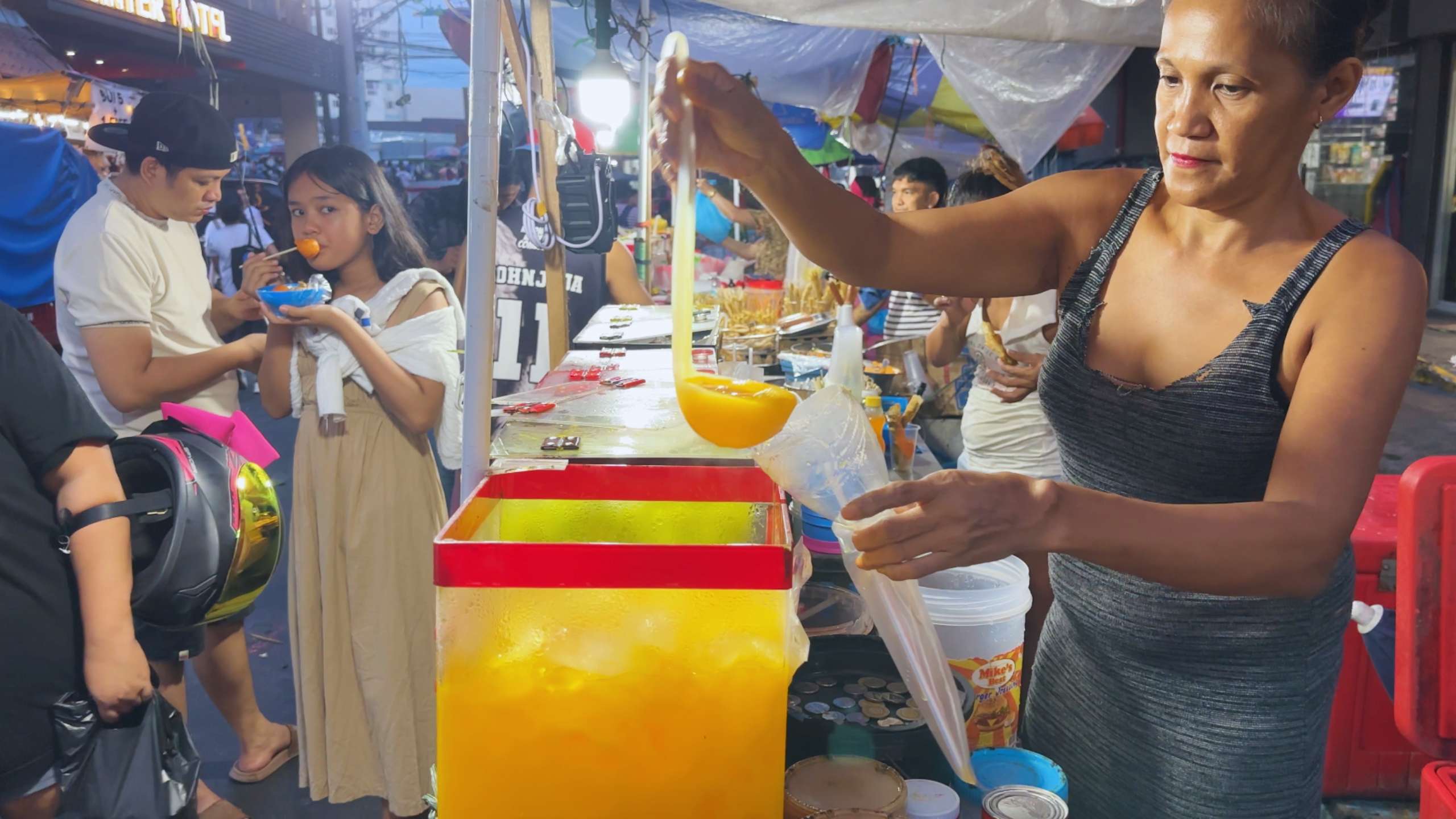 Vendor pouring a bright yellow juice as customers enjoy street food nearby.