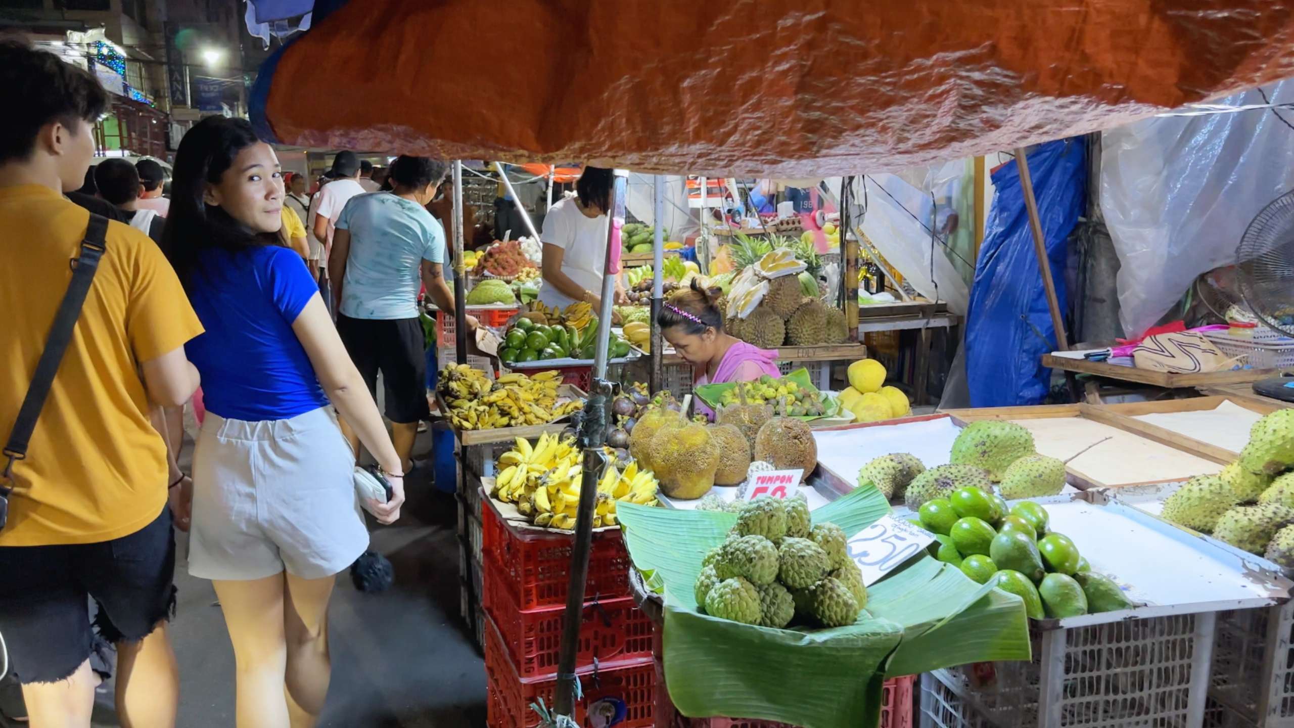 Young woman browsing through a market filled with exotic tropical fruits.