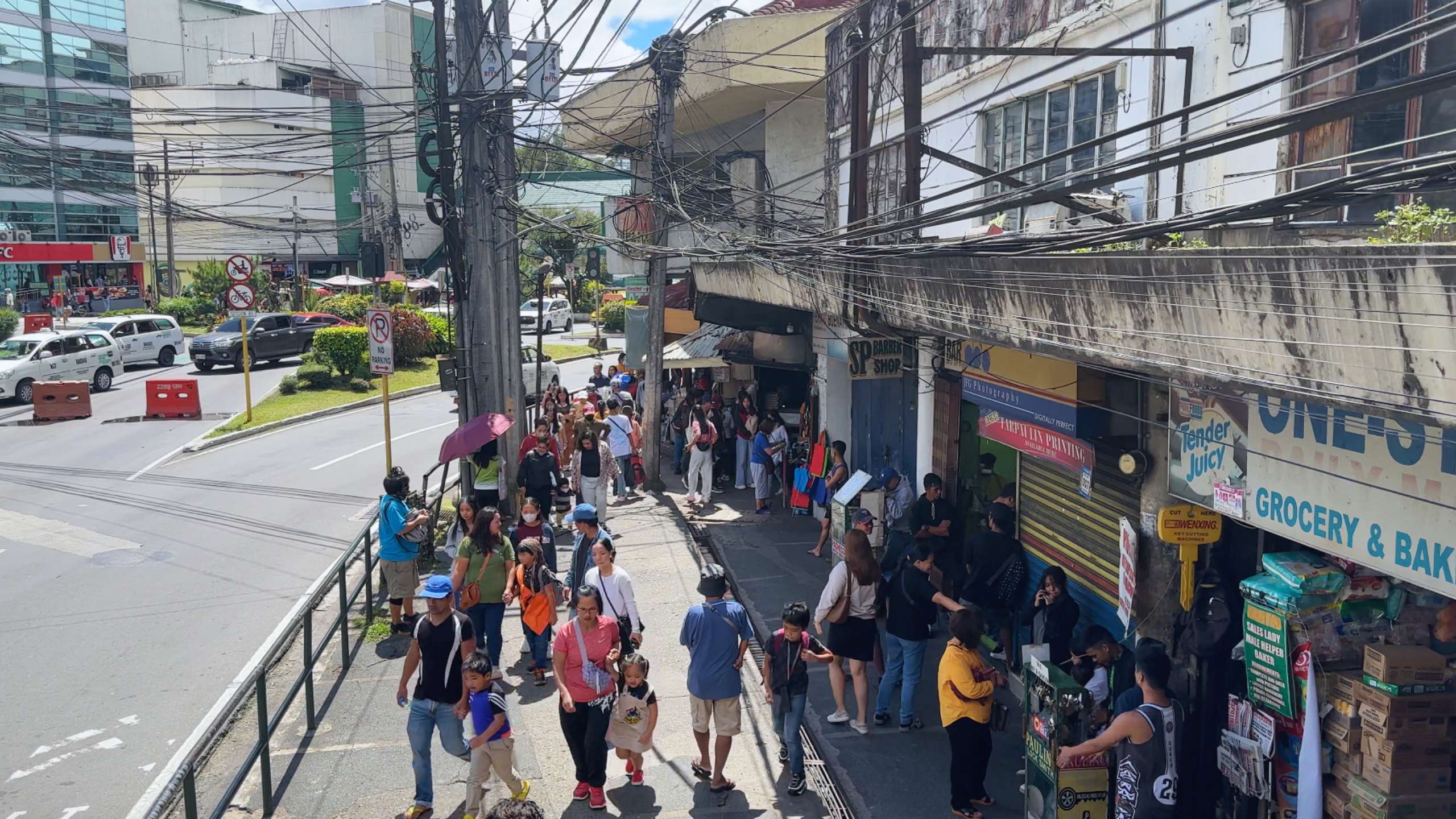 Busy sidewalk with locals and tourists passing by shops and market stalls.