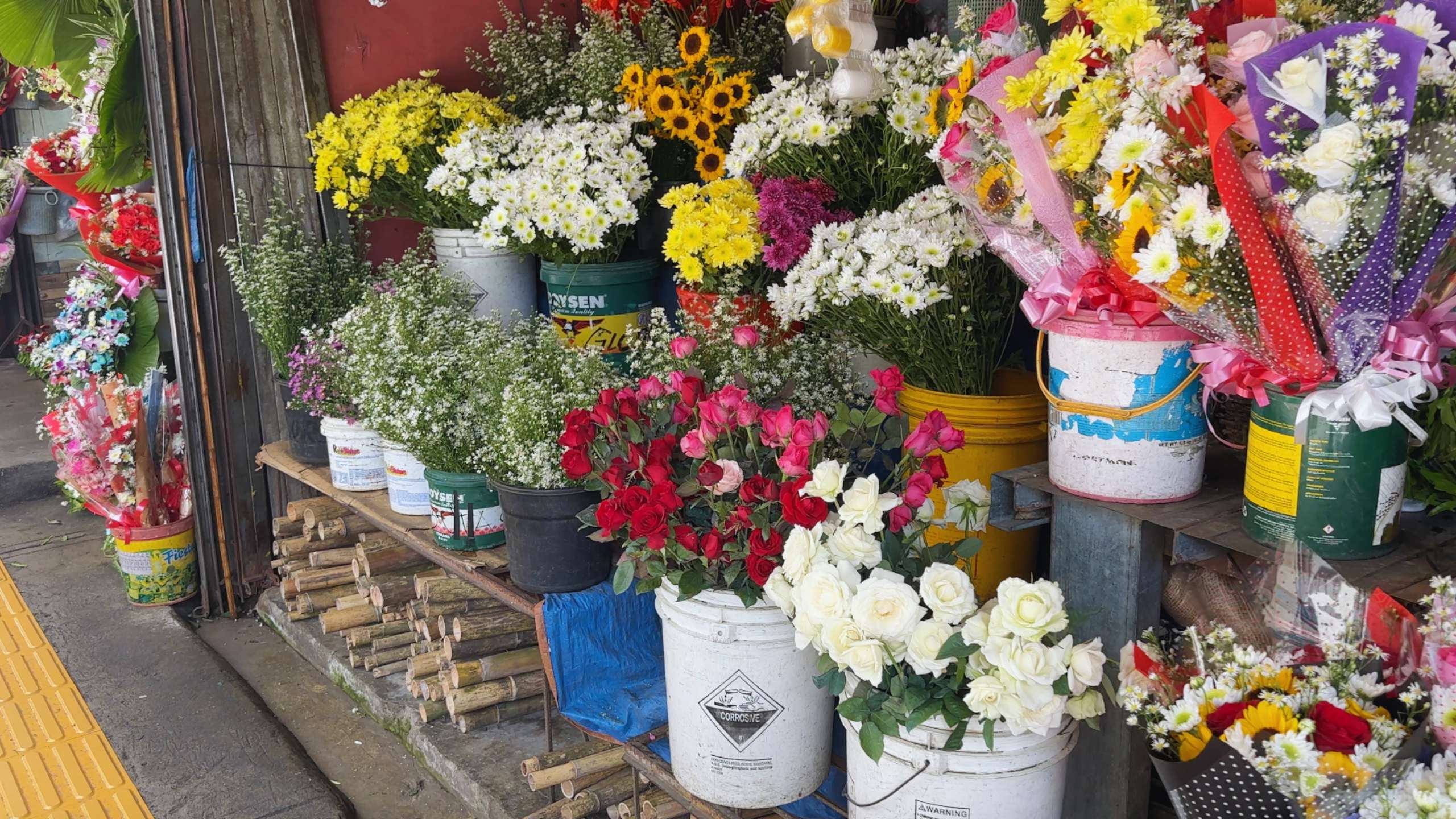 Bright, colorful flowers in buckets create a lively display at a market stall.