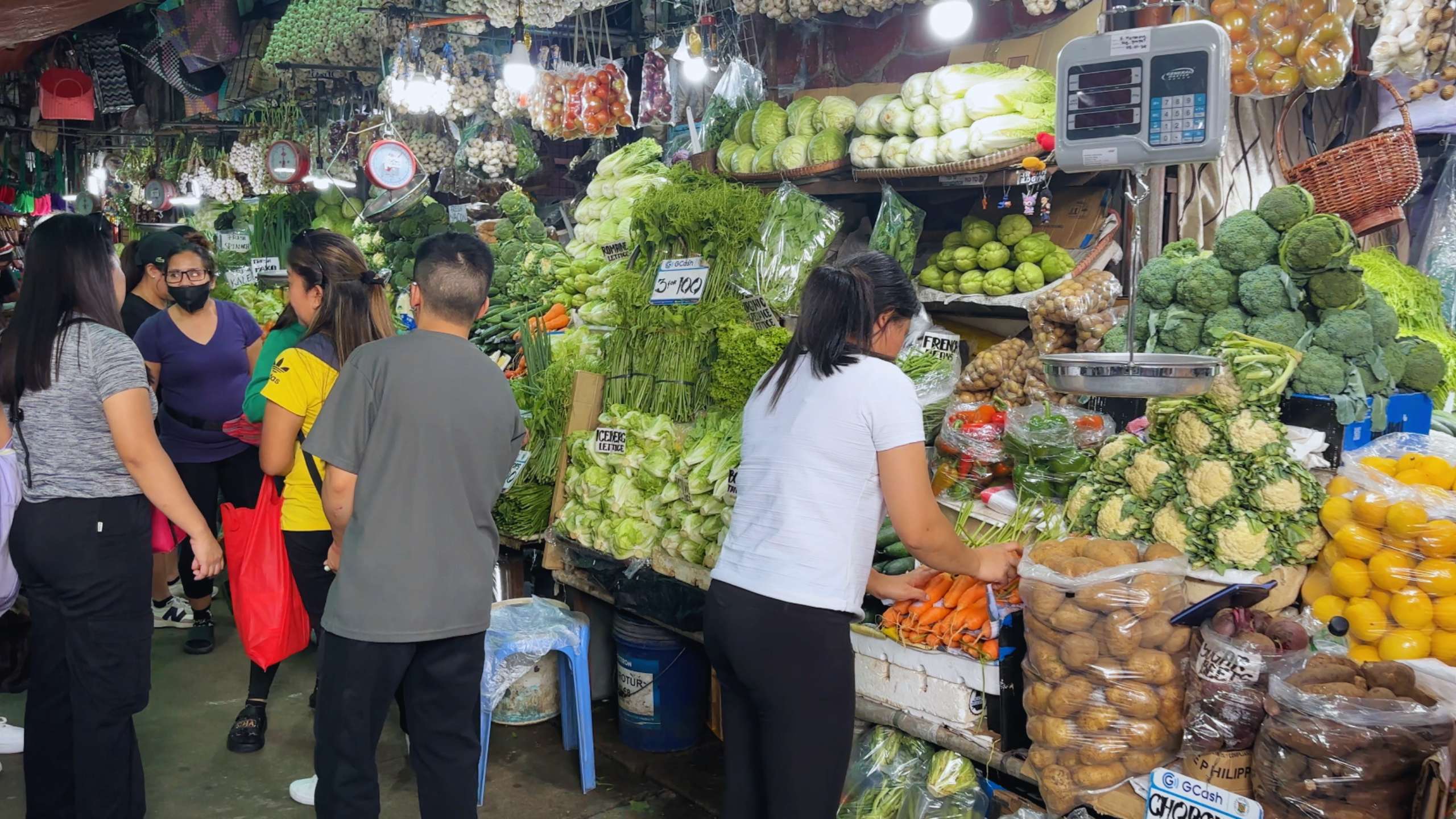 Shoppers browse through fresh vegetables in a bustling indoor market.